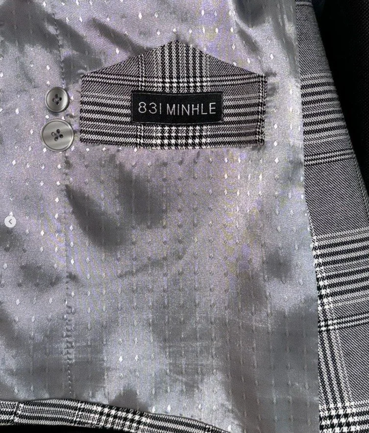 Close-up of the inside of a suit jacket with a black and white plaid lining and a label that reads "831 MINHLE." Two gray buttons are visible on the left side.