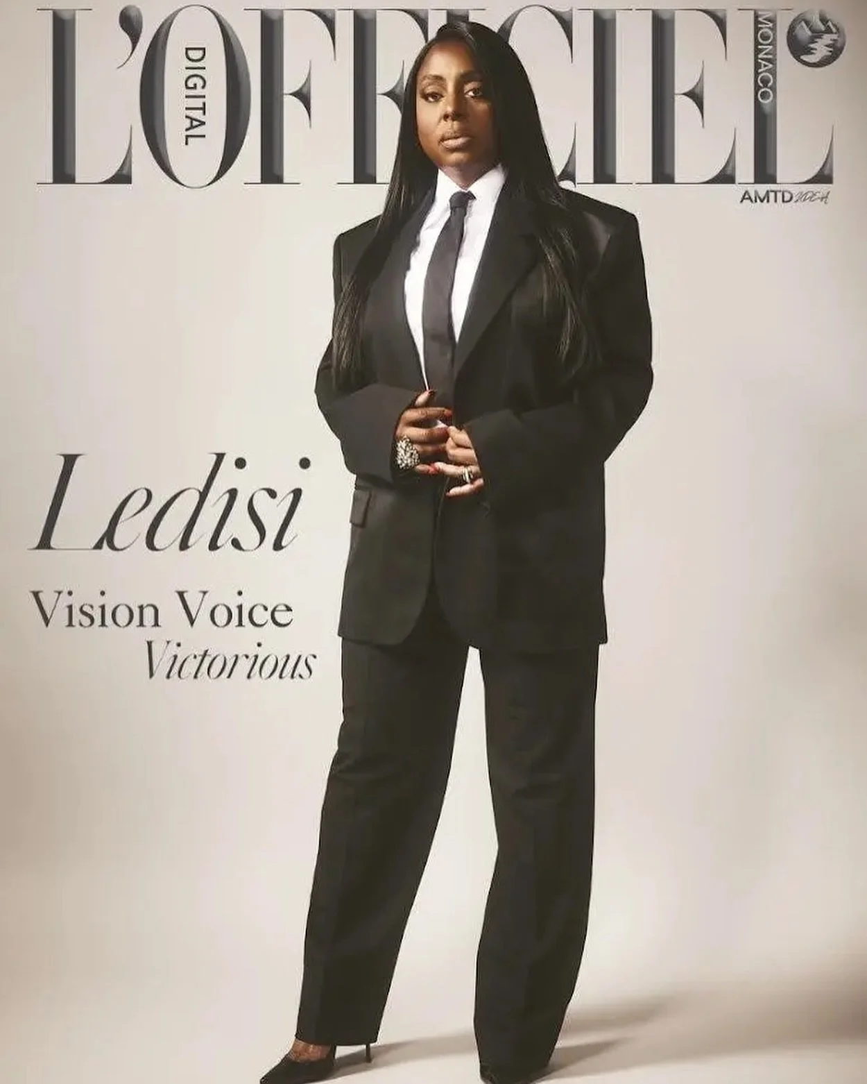 Magazine cover featuring a woman in a black business suit with a white shirt and black tie, standing against a backdrop with the title 'L'Officiel' and the name 'Lediši' along with the words 'Vision Voice Victorious'.