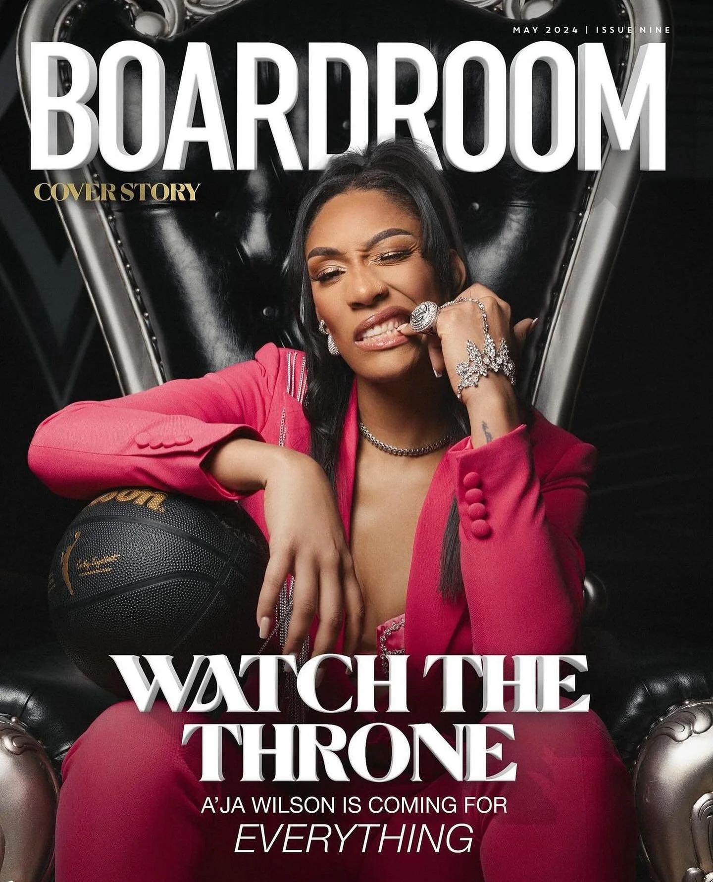 A woman in a pink suit sitting on a black throne-like chair, holding a basketball, with newspapers in the background. The cover headline reads 'Watch the Throne' and mentions A'ja Wilson.