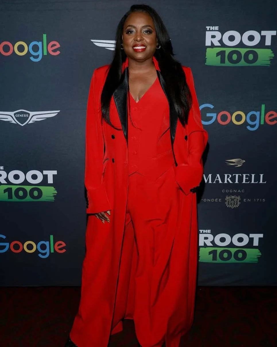 Woman in a red suit standing in front of a backdrop with logos of Google and the Roots 100.