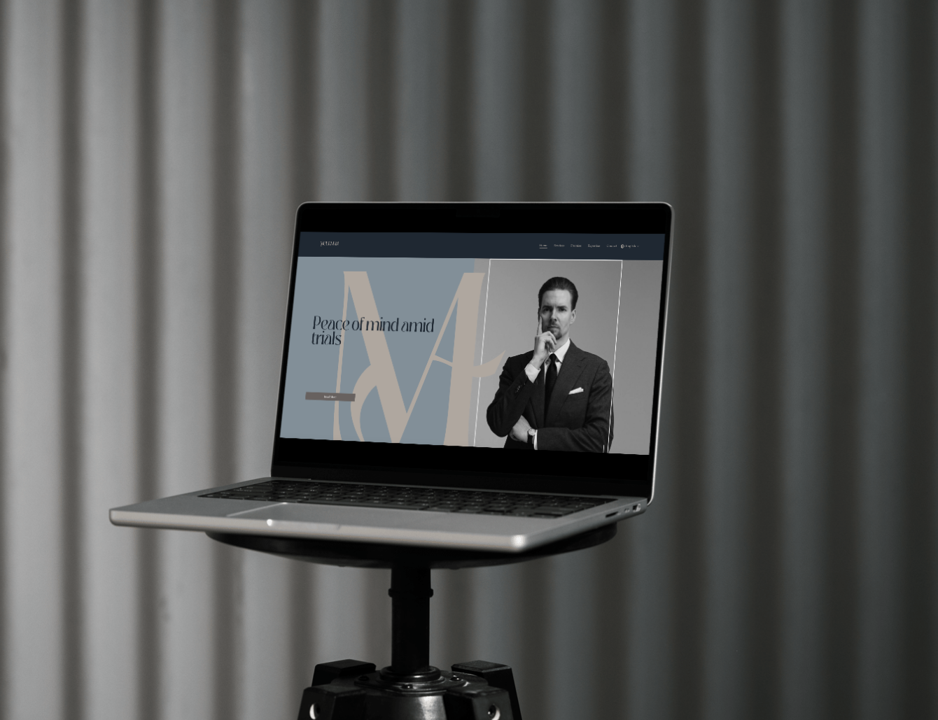 Laptop on a stand displaying a website with a man in a suit and the text 'Peace of mind amid trials'.