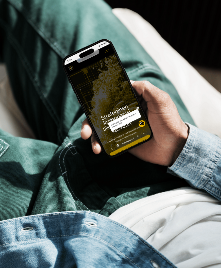 Person sitting and using a smartphone with a black and yellow app interface that displays text in a foreign language, wearing blue jeans and a light-colored shirt.