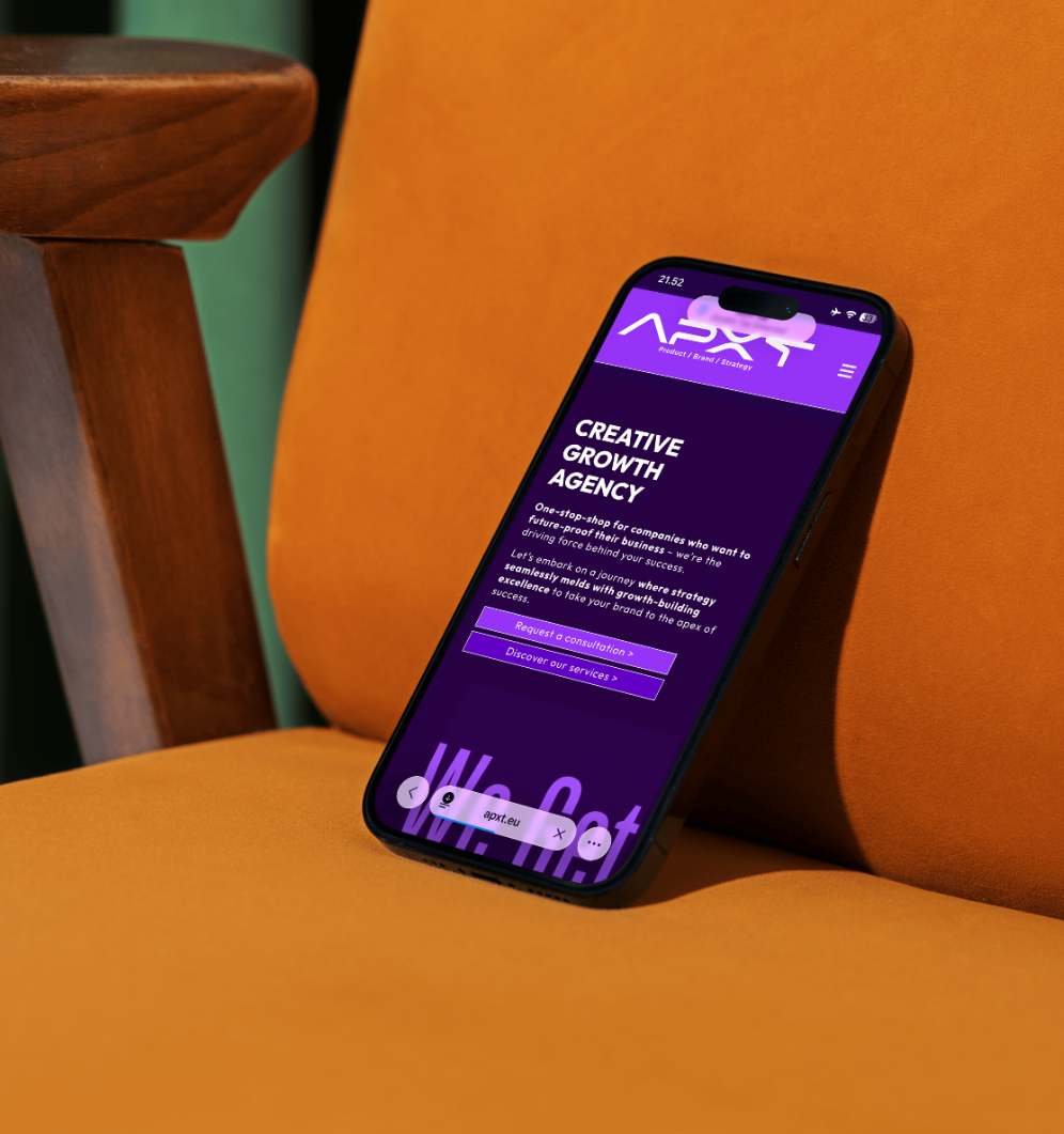 Smartphone displaying a website for a creative growth agency, resting on an orange couch with a wooden armrest nearby.