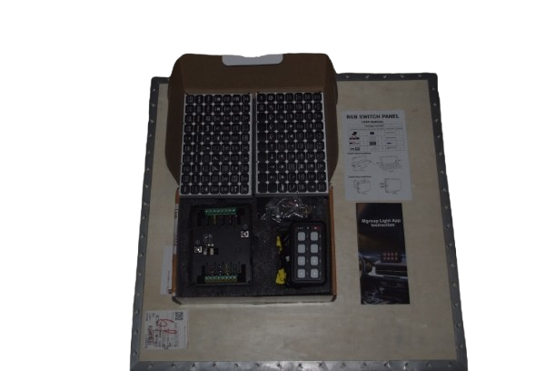 Open box containing LED switch panel, remote control, wiring, and instruction sheet on a flat surface.