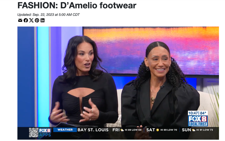 Two women sitting on a TV set during a fashion segment about D'Amelio footwear, with a colorful sunset background on a screen behind them.