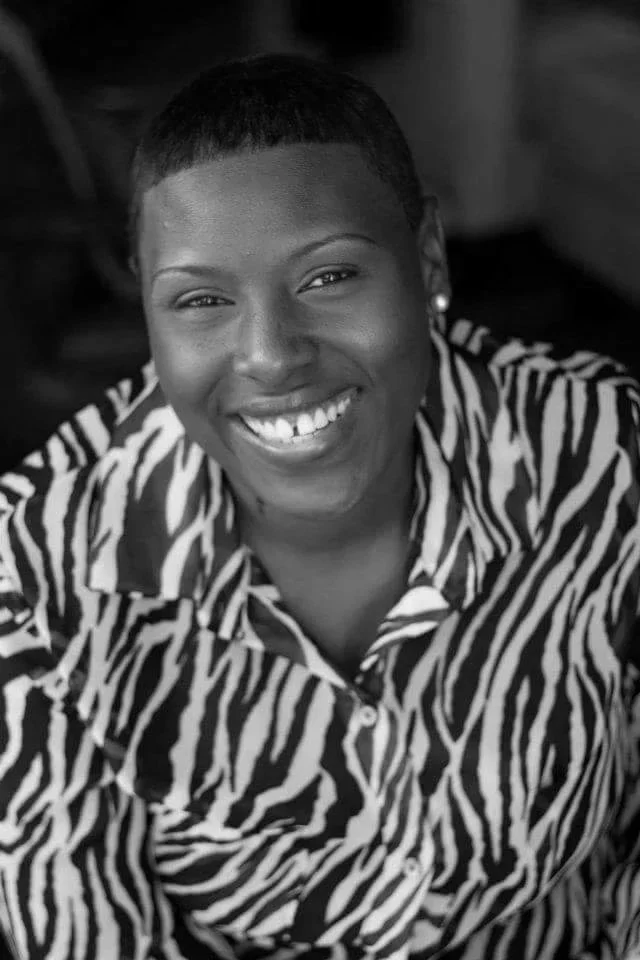 A smiling African American woman with short hair, wearing a zebra print shirt, in black and white photograph.