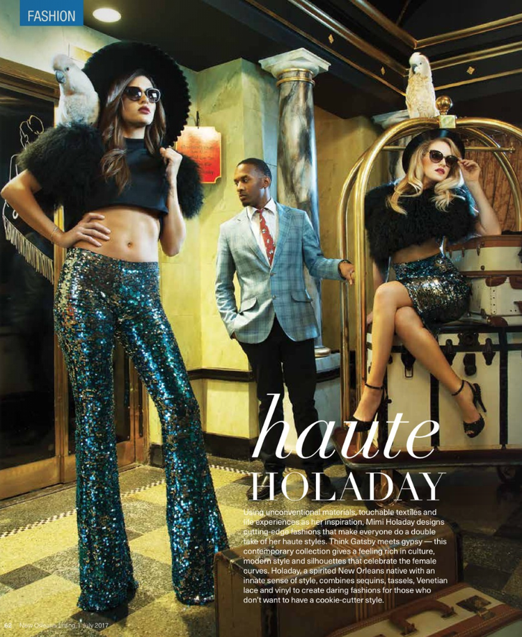 Three women and one man in a fashionable, stylish setting with vintage decor. Two women wear shiny sequin outfits and sunglasses; one is sitting on a vintage-style barber's chair, and the other stands with one hand on her hip. The man stands between 