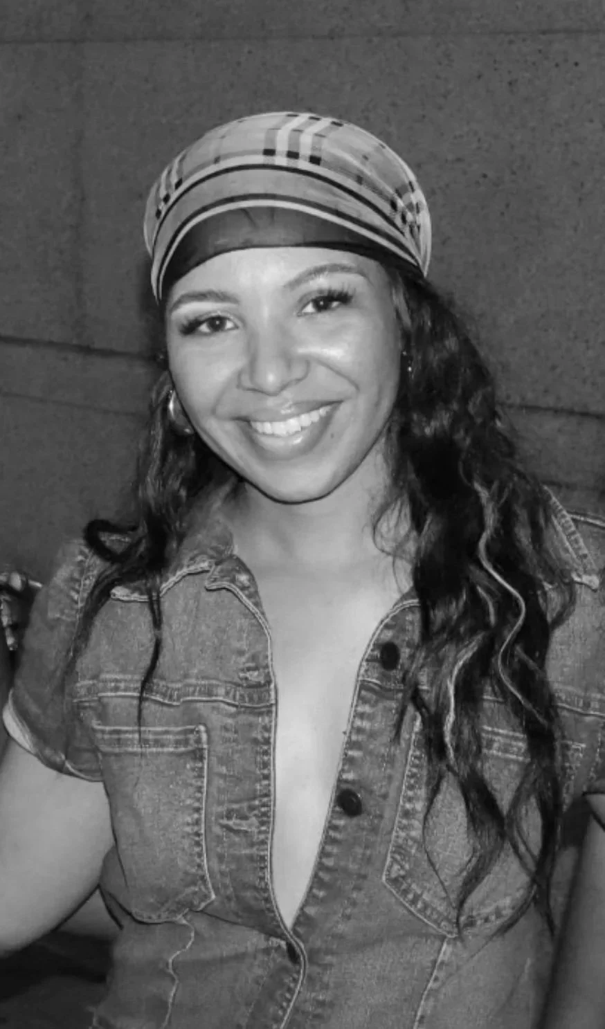 A smiling woman wearing a patterned headscarf and a denim top with a deep neckline.