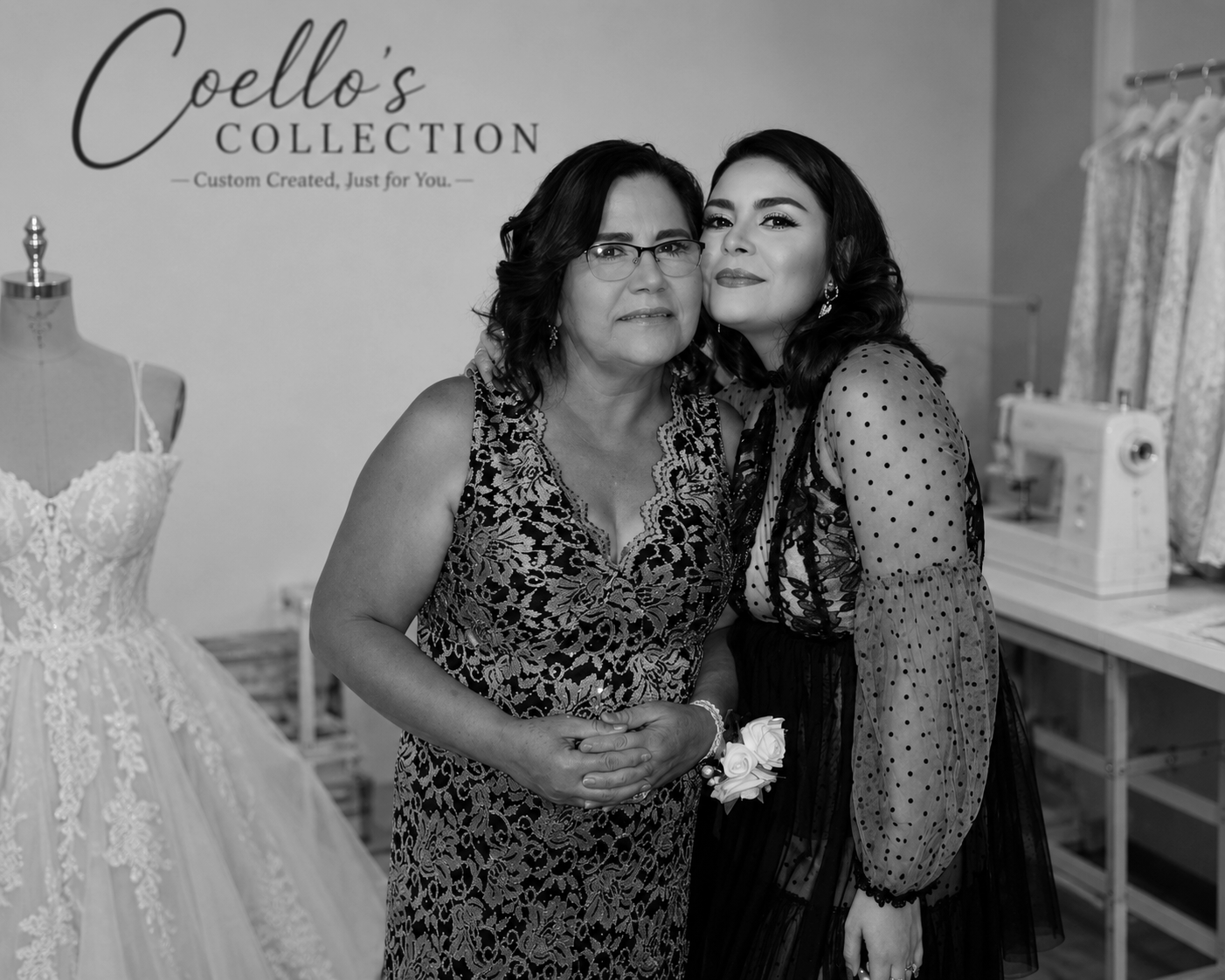 Two women hugging at a wedding dress shop, with the shop's sign 'Coello's Collection' in the background. One woman appears older and is wearing glasses and a lace dress, while the younger woman has dark hair and is dressed in a sheer polka-dot dress.