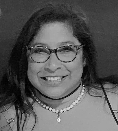 A woman wearing glasses, a pearl necklace, and smiling in a black-and-white photo.