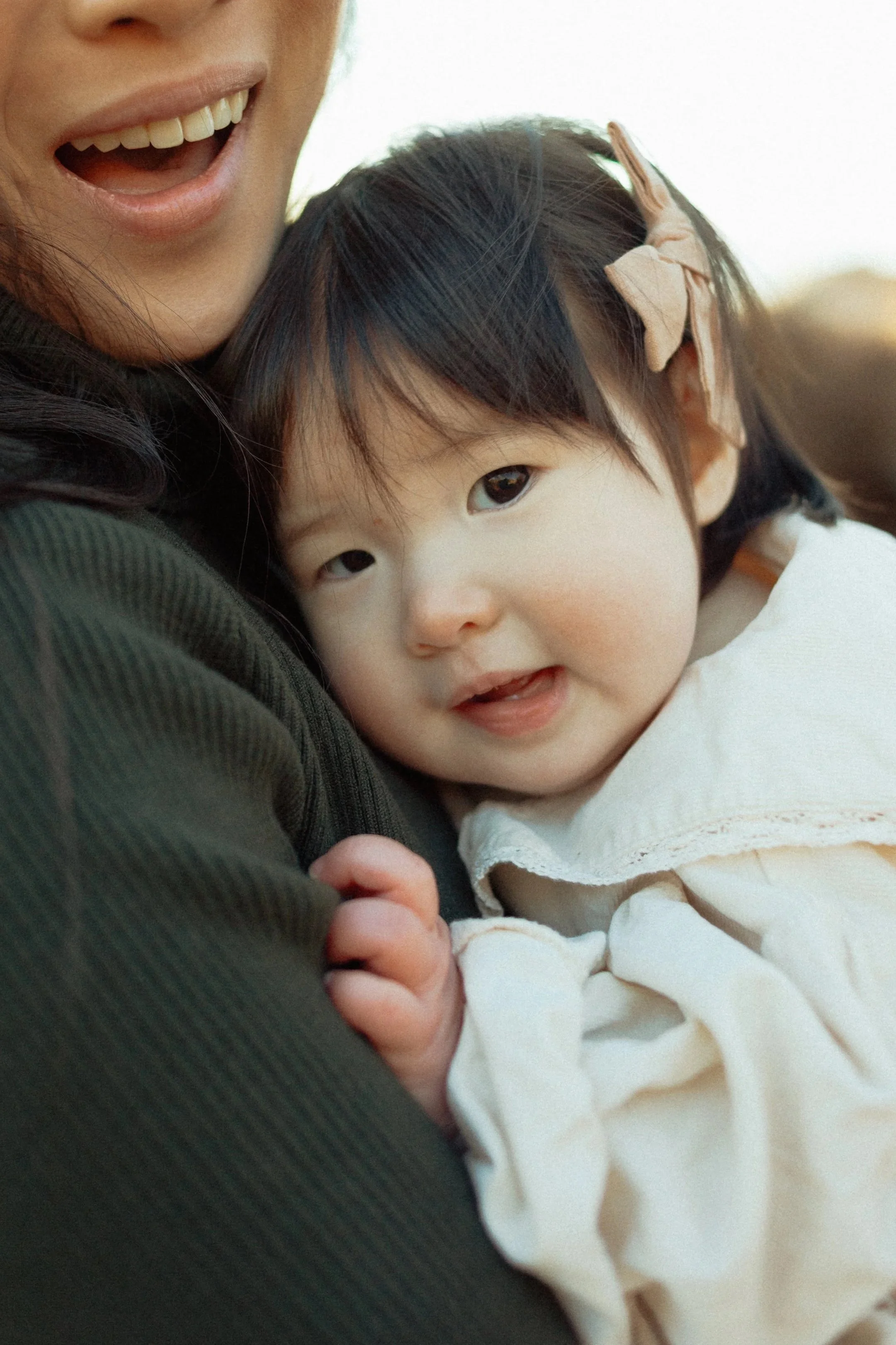 A woman holding a young girl close, both smiling and looking at the camera. Family photoshoot. 