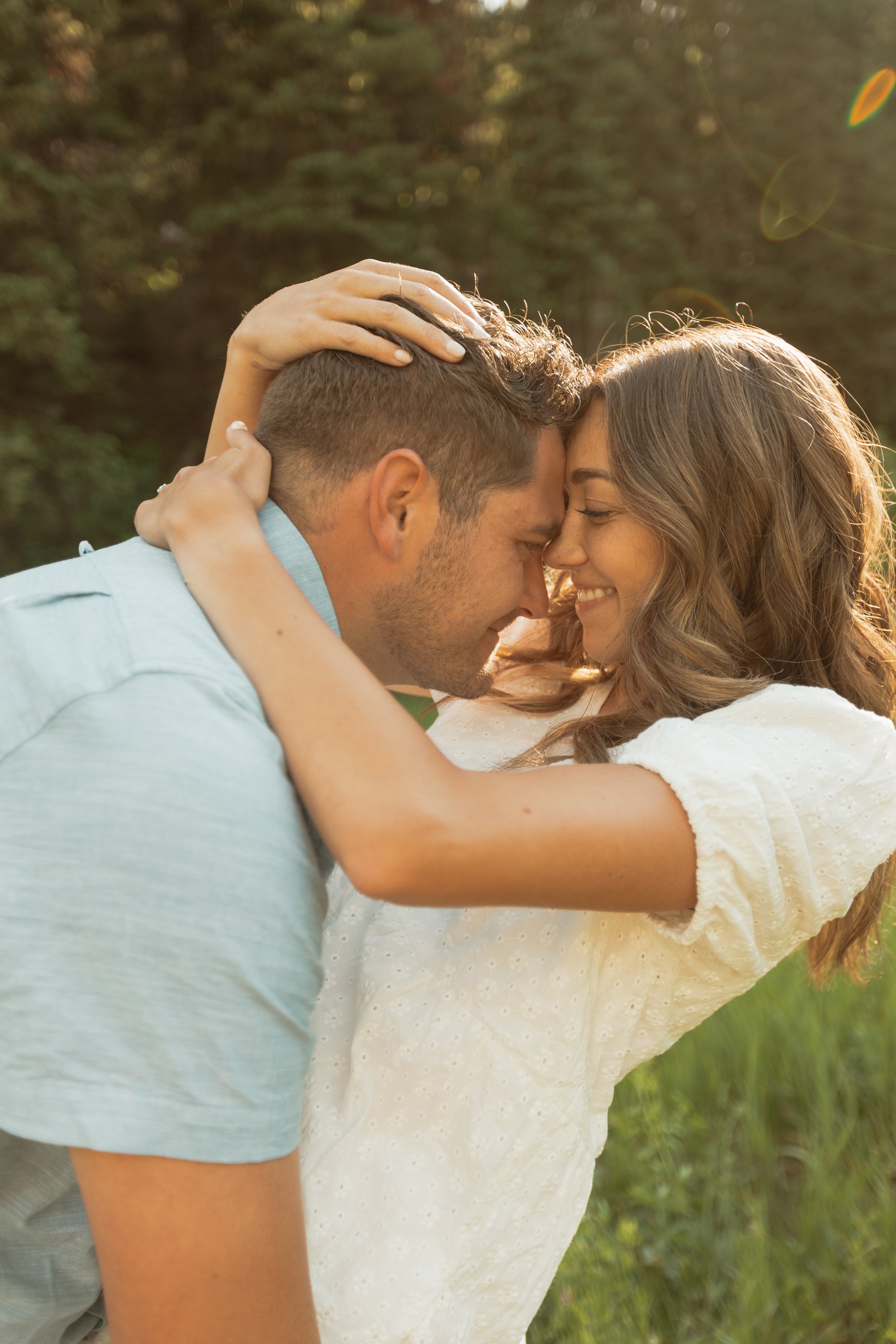 A couple embraces outdoors during sunset, touching foreheads and smiling, with a blurred green background in Millcreek Canyon, Salt Lake City Utah.