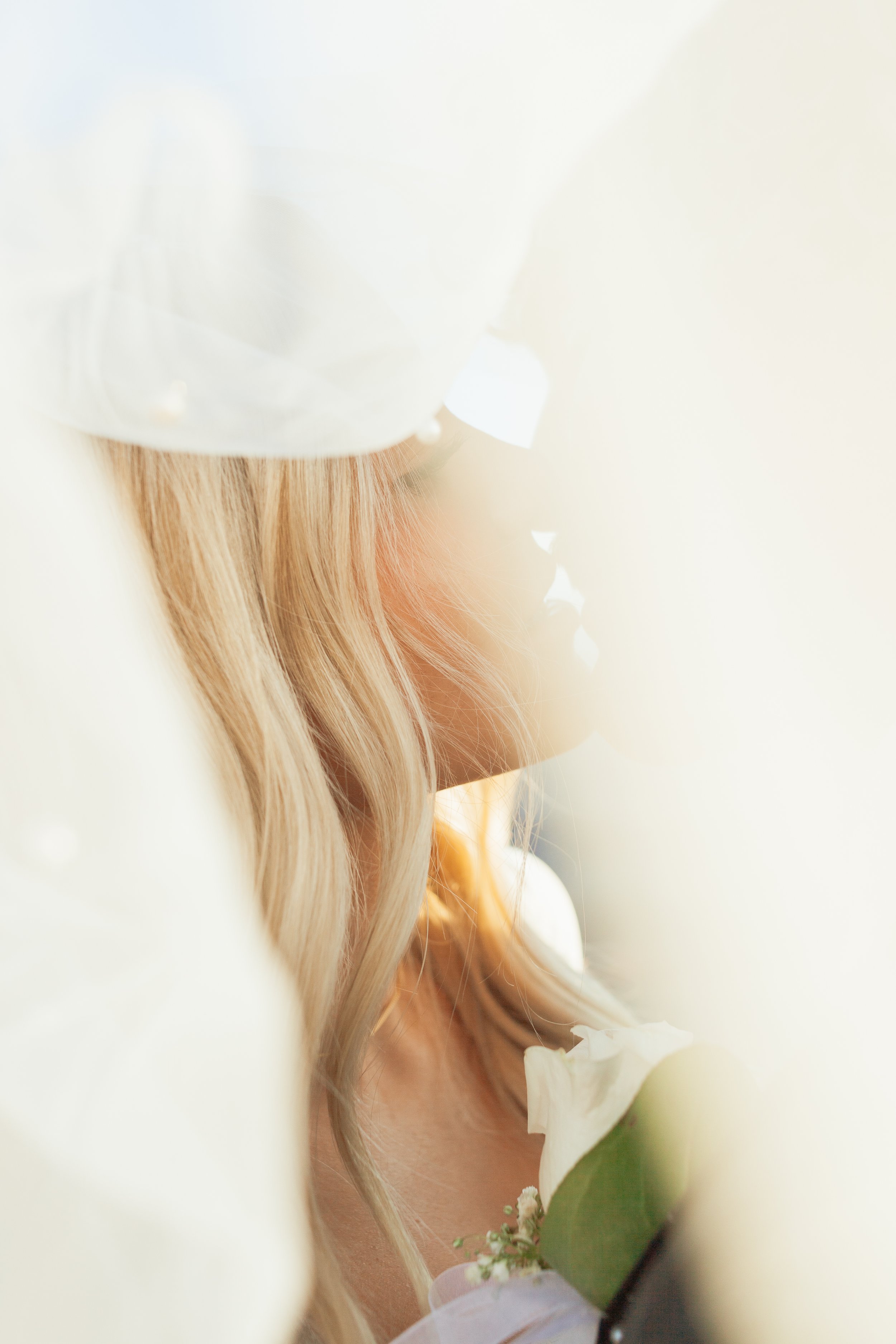 A bride with long blonde hair holding a white flower, partially obscured by white fabric or curtains, in warm sunlight at Dead Horse Point State Park in Moab, Utah.