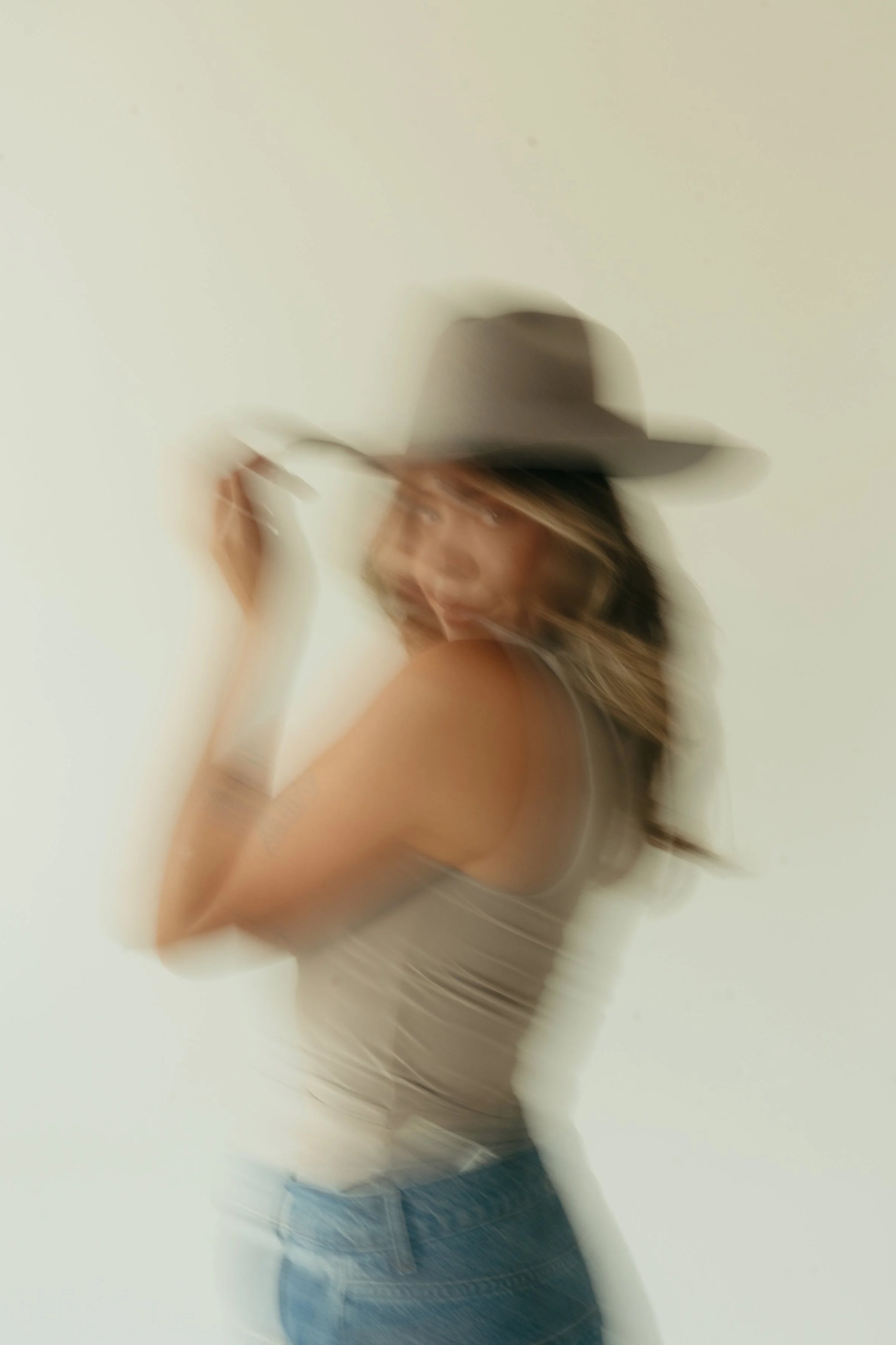 A woman wearing a hat and striped top, holding the brim of her hat, with a motion-blurred effect.