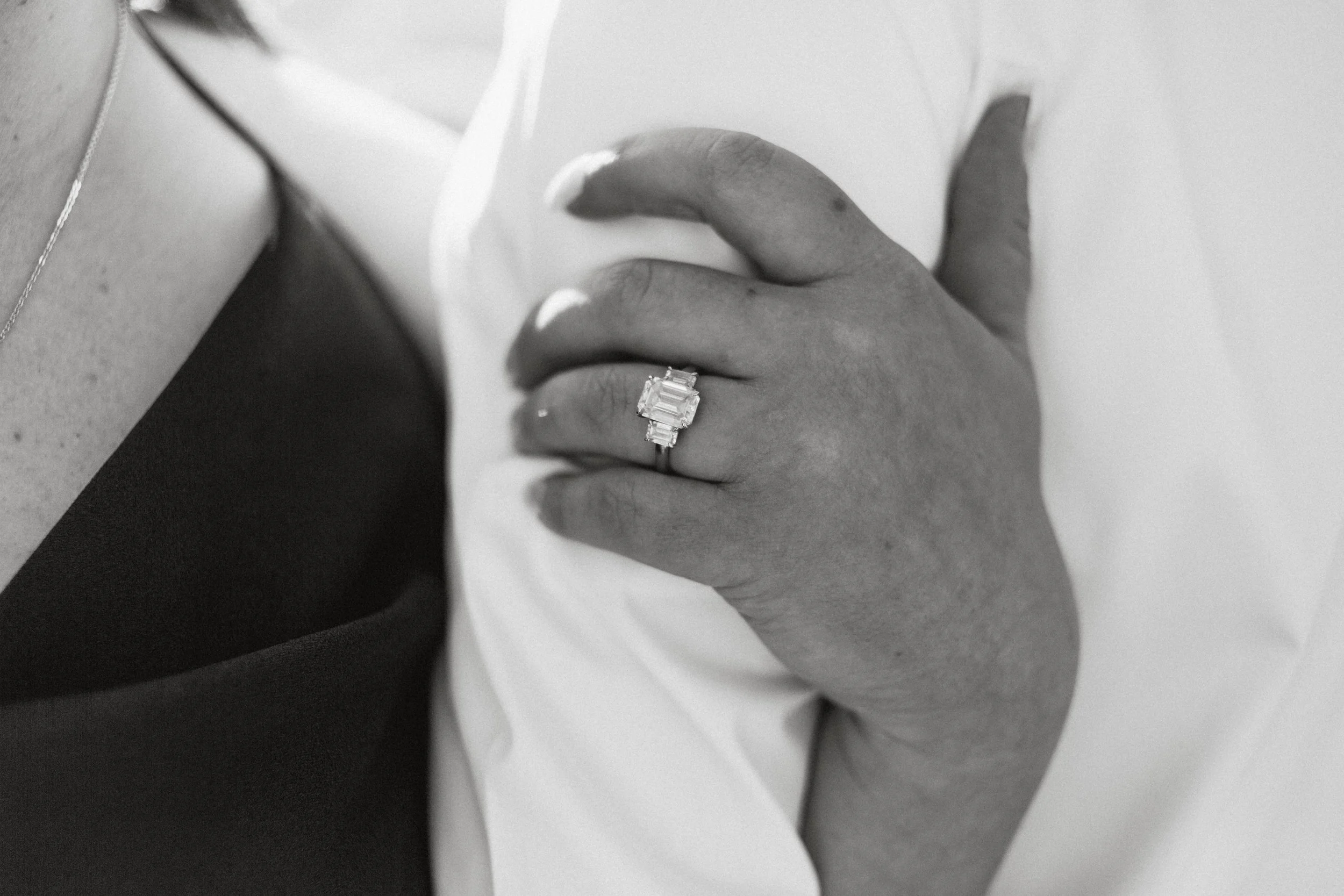 Close-up of a hand with an engagement ring featuring multiple rectangular diamonds, resting on fabric.