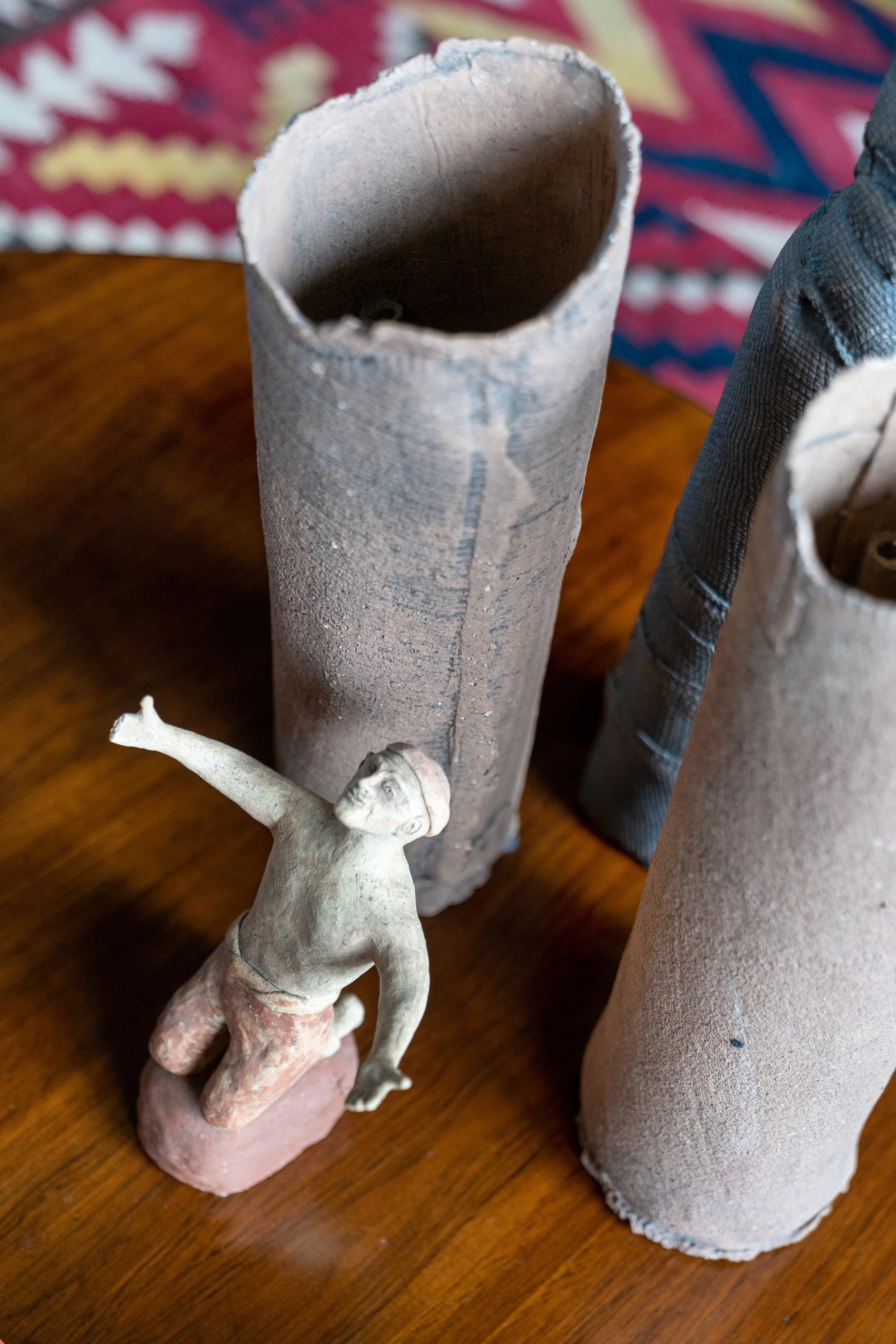 Two large cardboard tubes standing upright on a wooden surface, with a small figurine of a man kneeling and appearing to reach out or gesture.