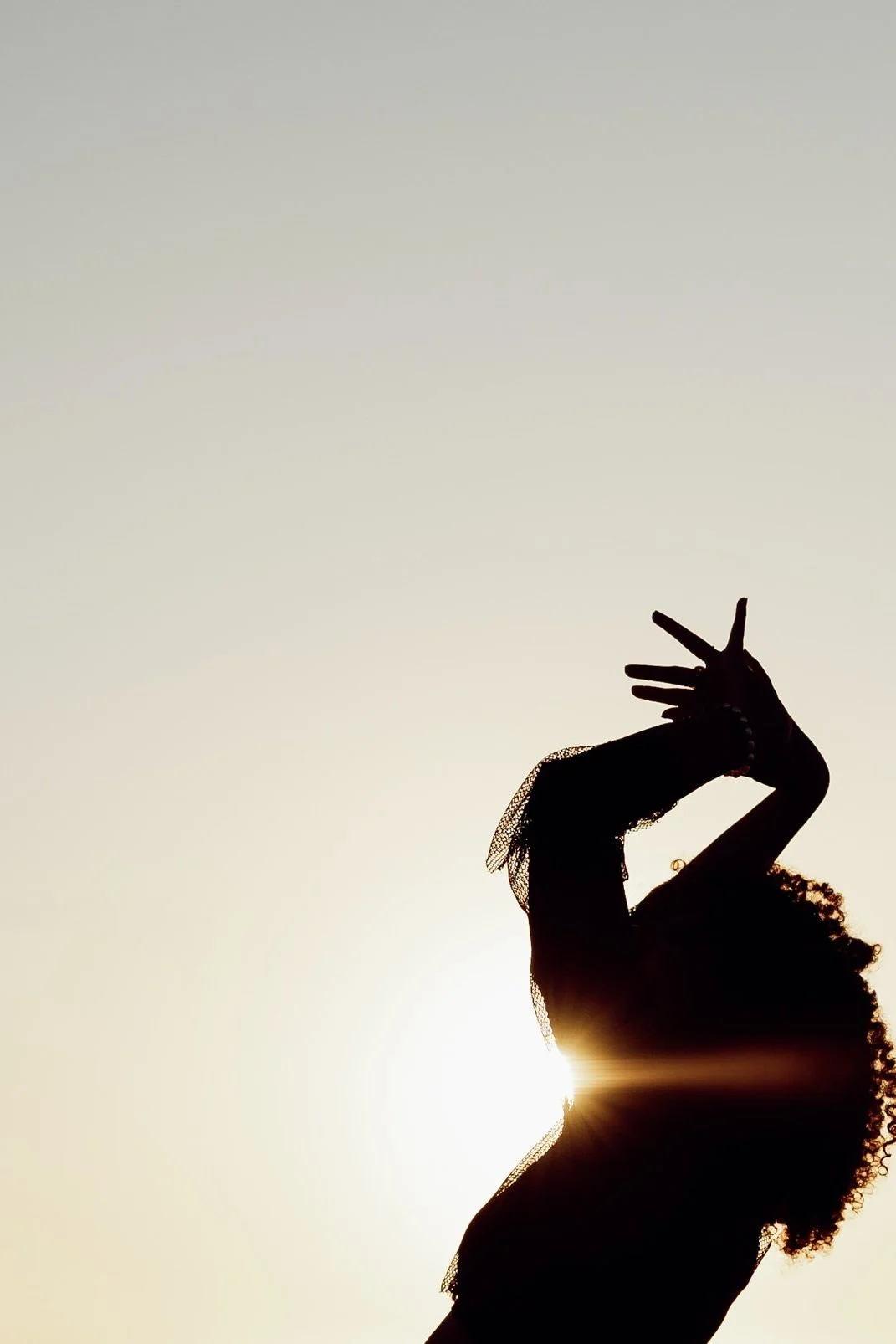 Silhouette d'une femme avec des cheveux bouclés faisant un signe de paix avec la main, derrière le soleil