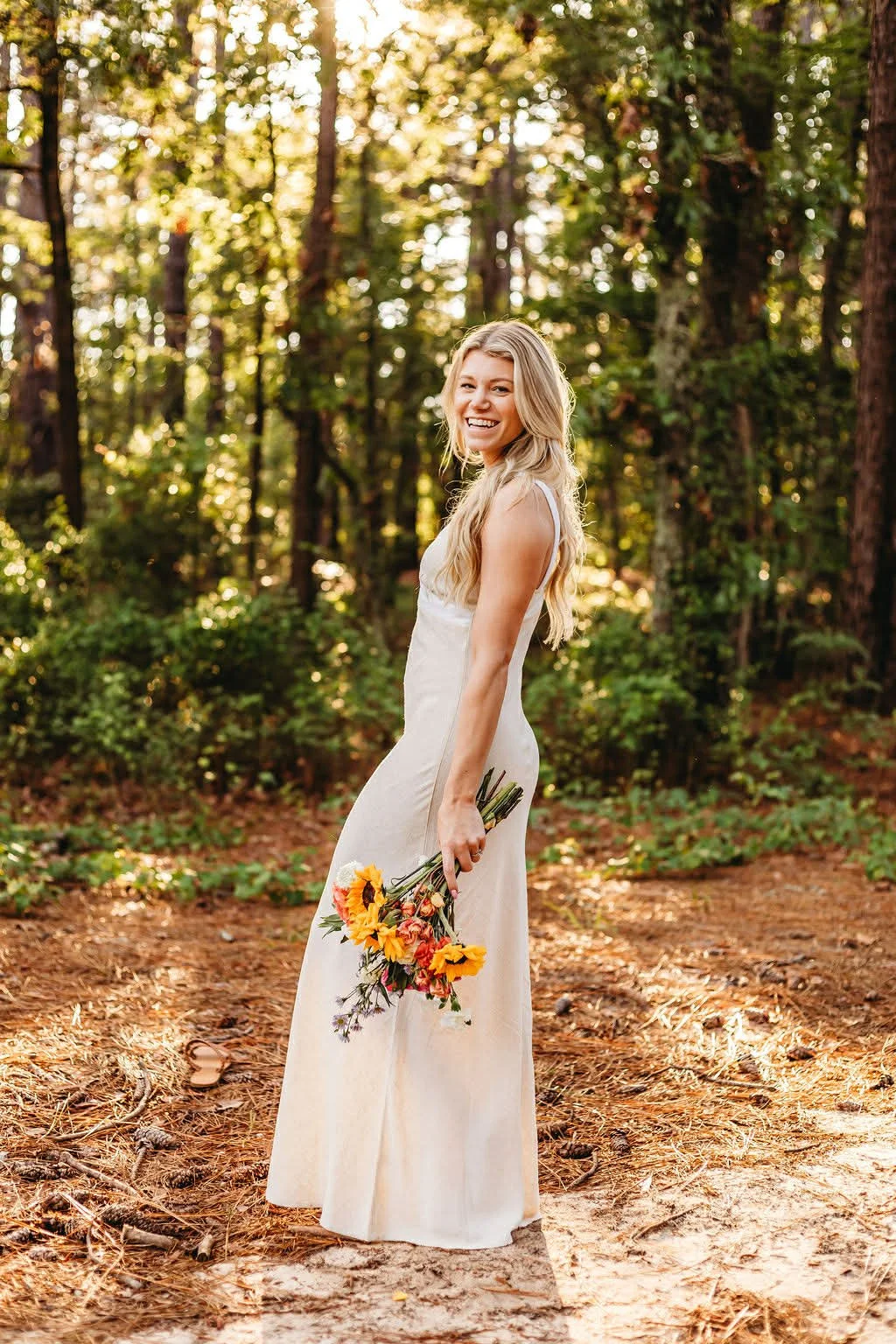 Florist smiling in woods displaying custom bouquet of sunflowers and daisies