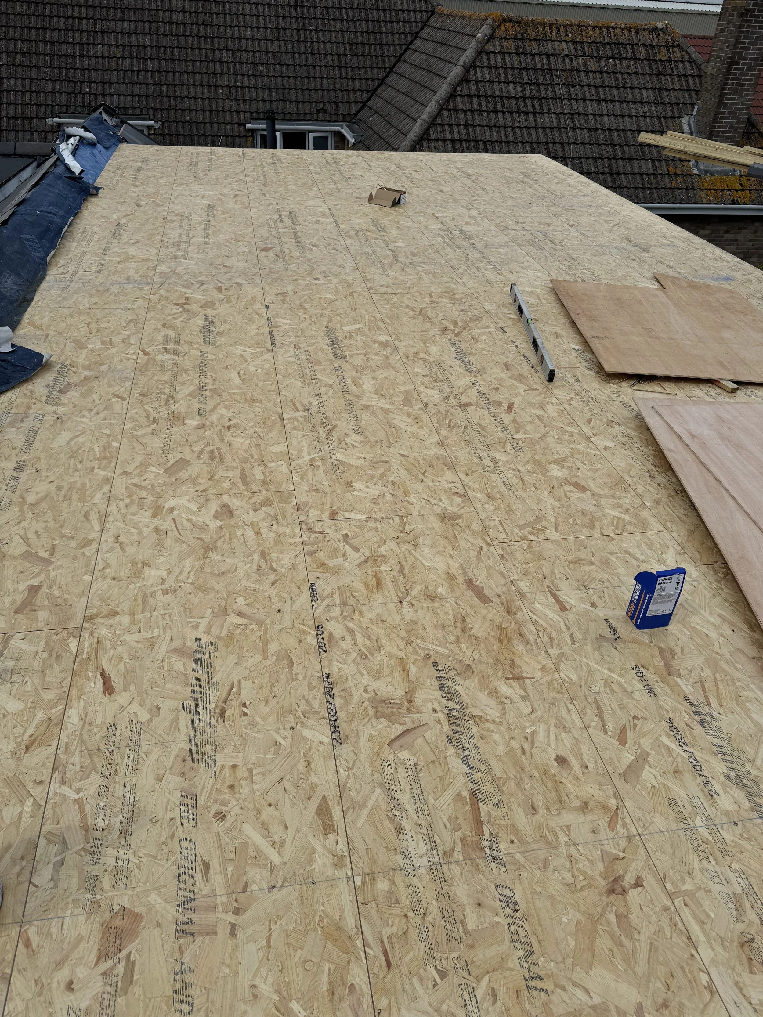 Construction site with OSB plywood sheathing on a roof under construction, with roofing materials and tools visible.