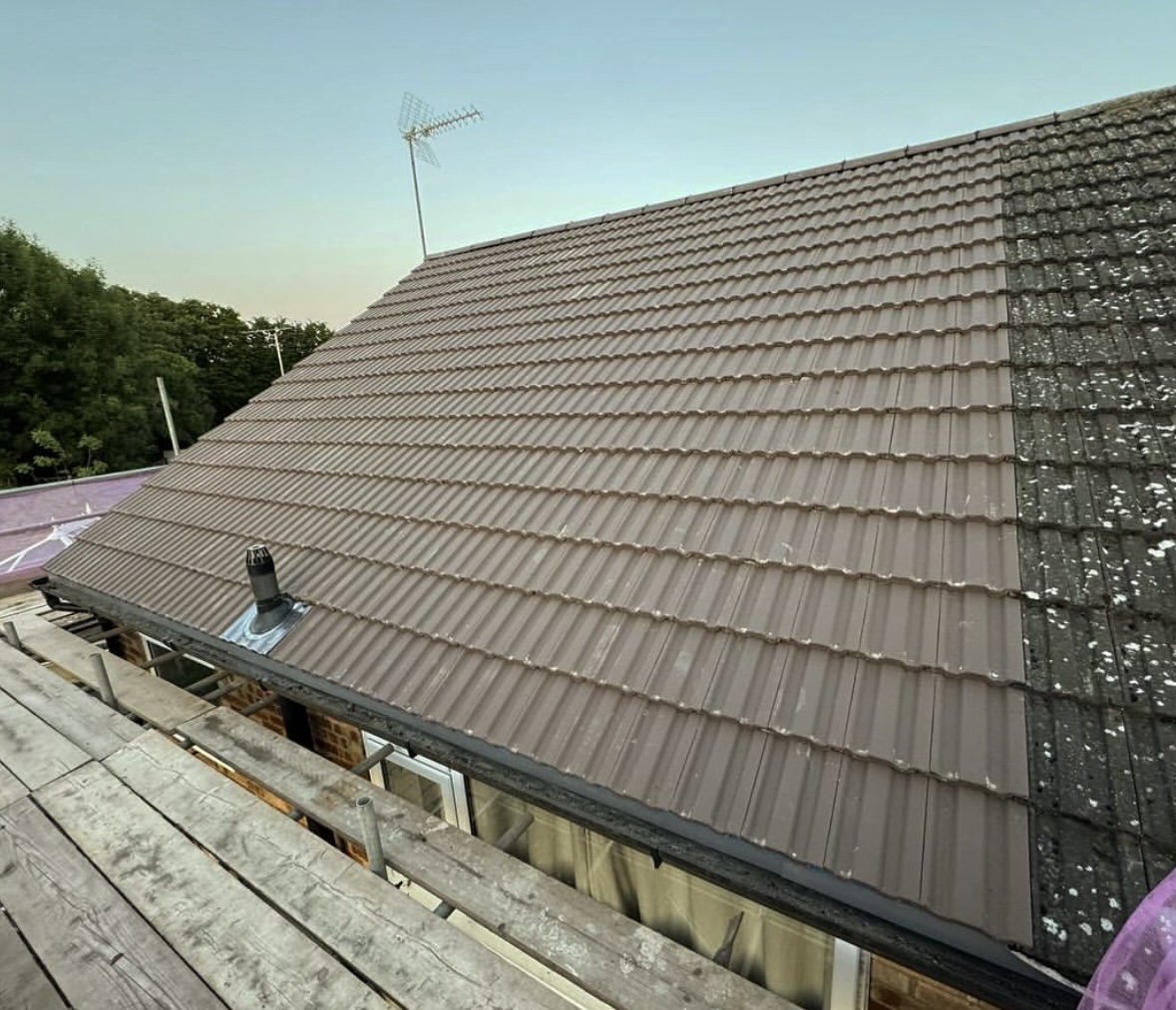 View of a sloped roof with beige and black roofing tiles, a chimney pipe, and an antenna, with part of the roof under construction in the foreground.