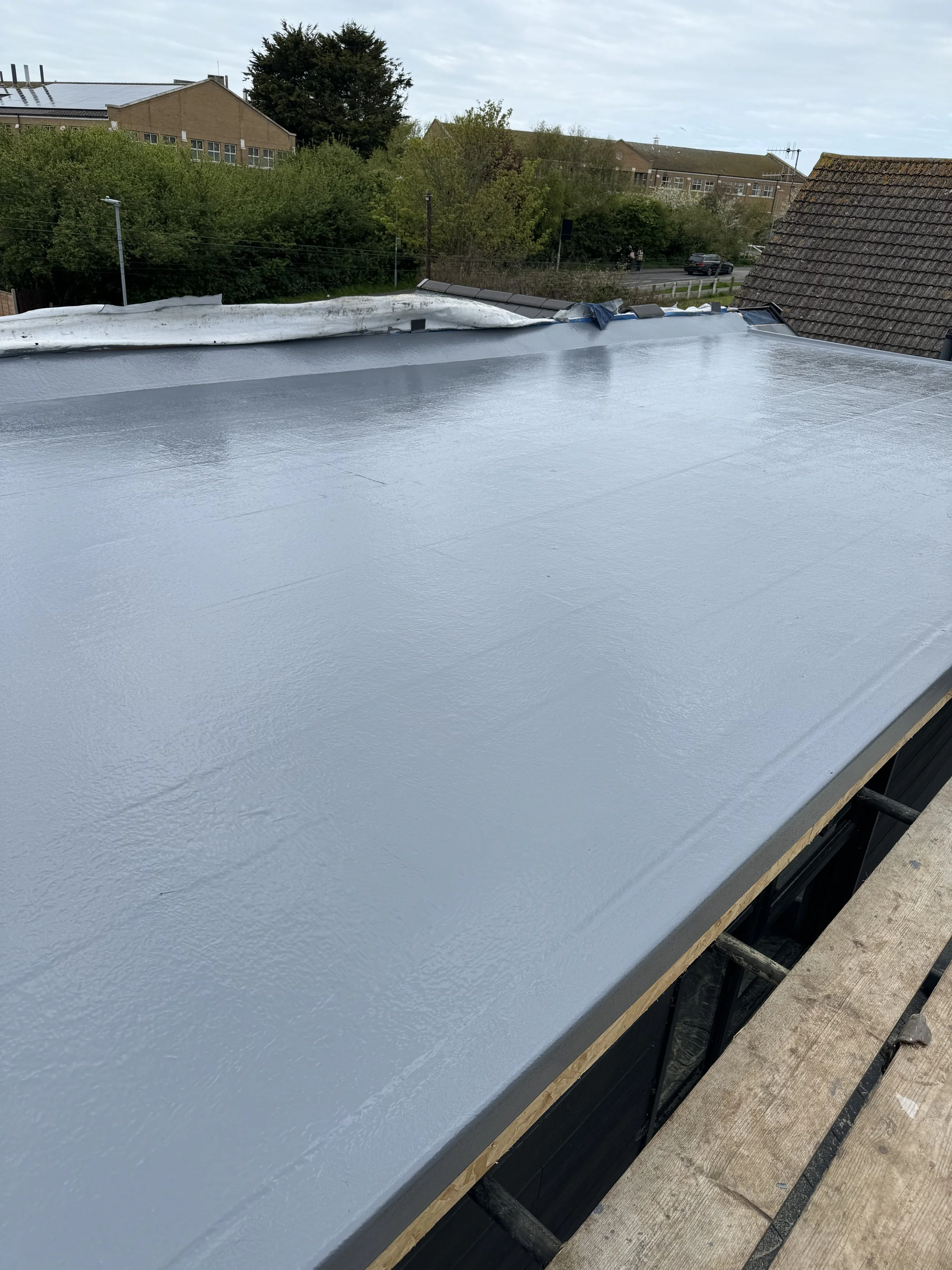 Freshly painted flat roof with a light gray, smooth, reflective surface, surrounded by some trees and buildings in the background.