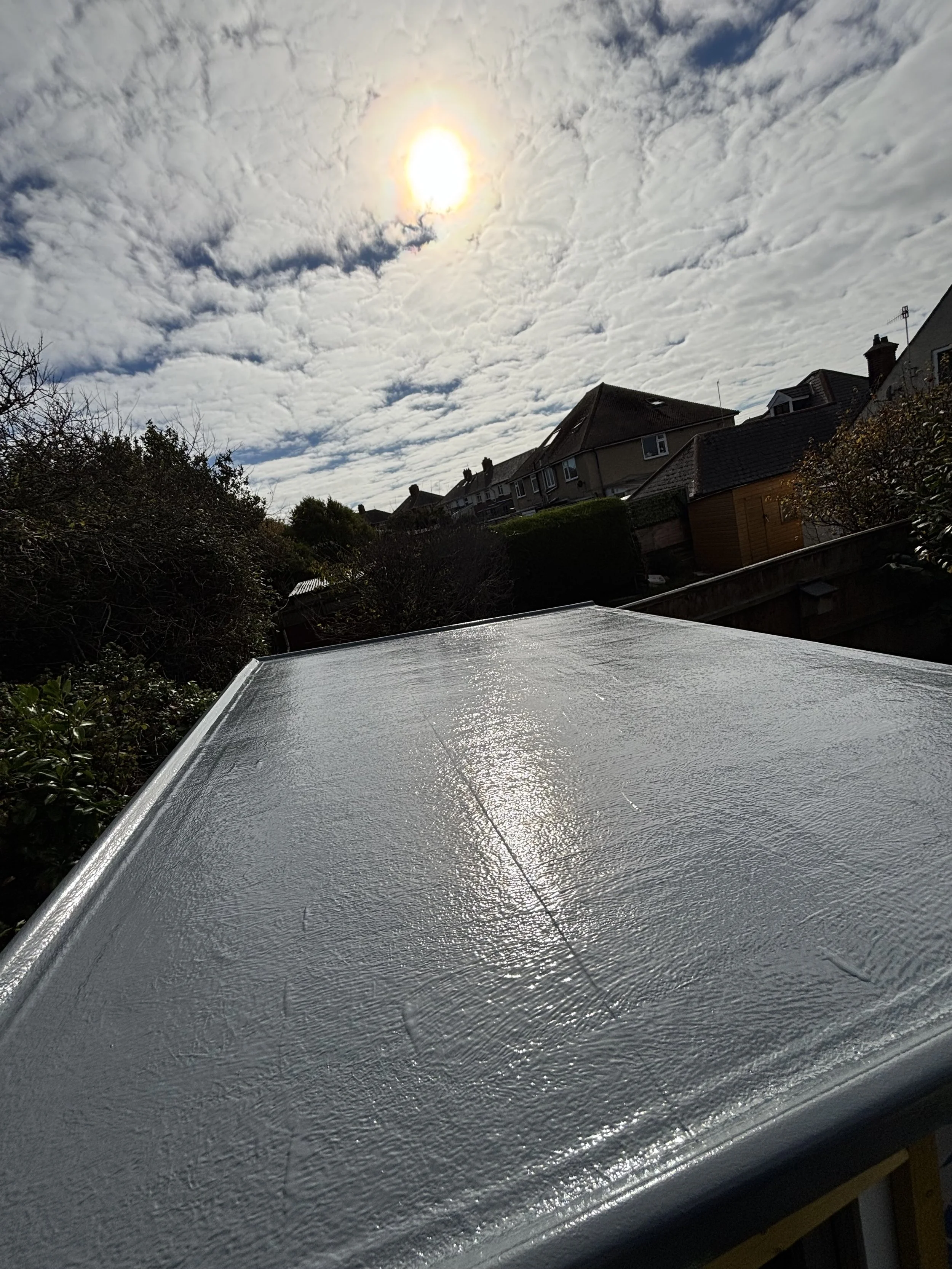 Close-up of a shiny, silver metal surface with a textured finish, outdoors under a partly cloudy sky with the sun overhead.