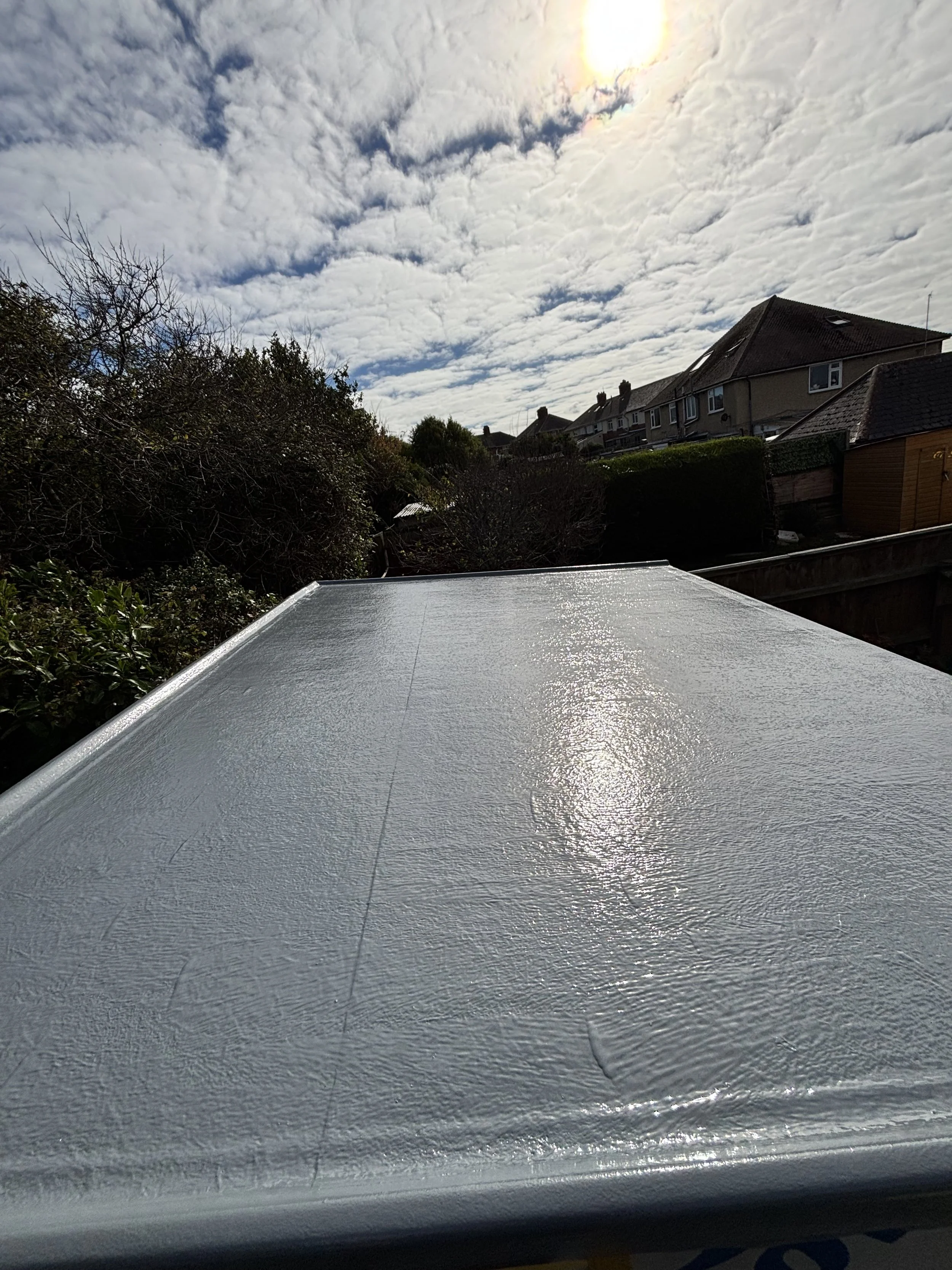 Close-up of a white, textured metallic surface with sunlight reflecting off it, outdoors under a partly cloudy sky with some clouds and sunlight.