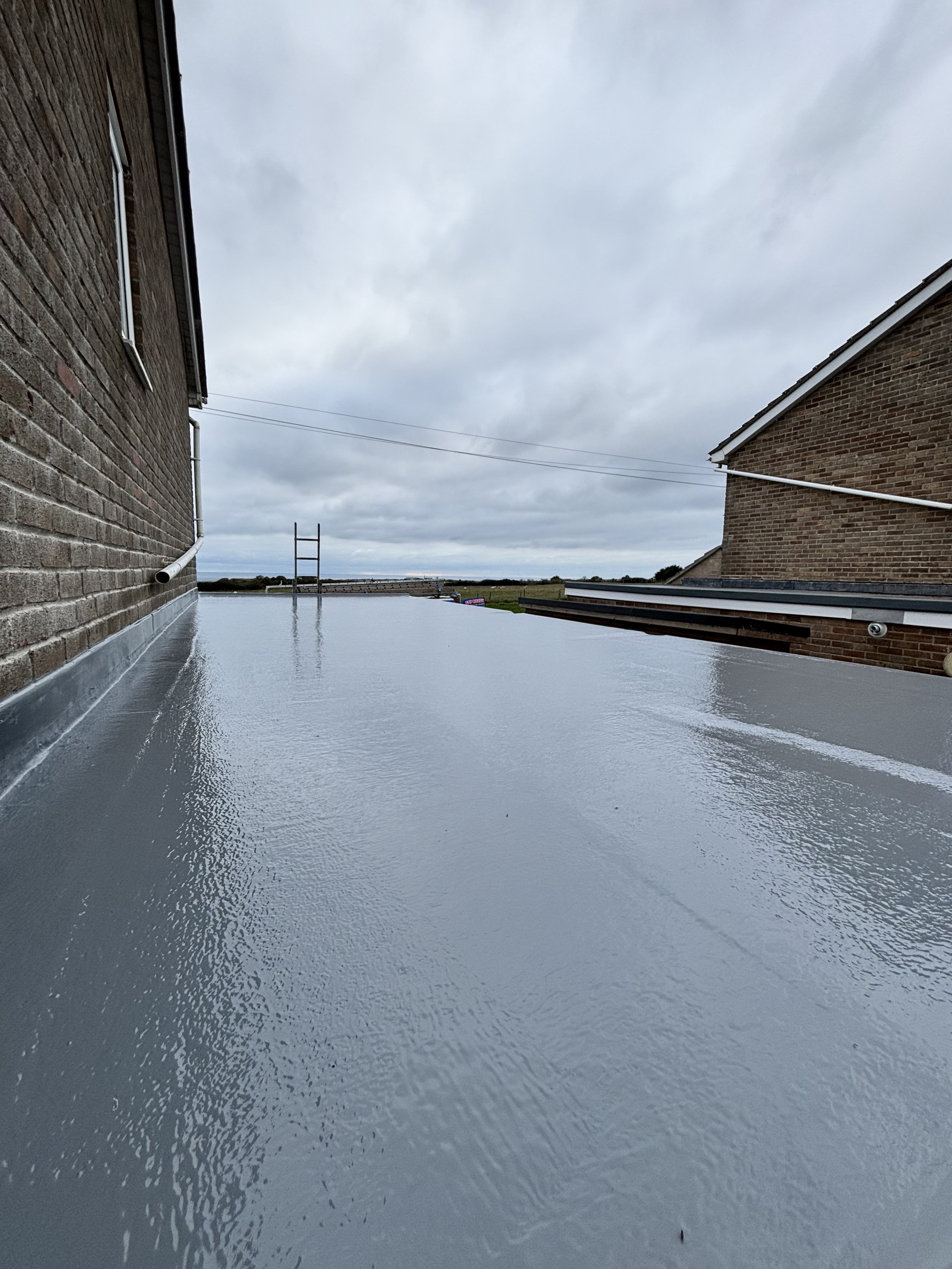 Flat roof with reflective coating between two brick buildings under a cloudy sky.