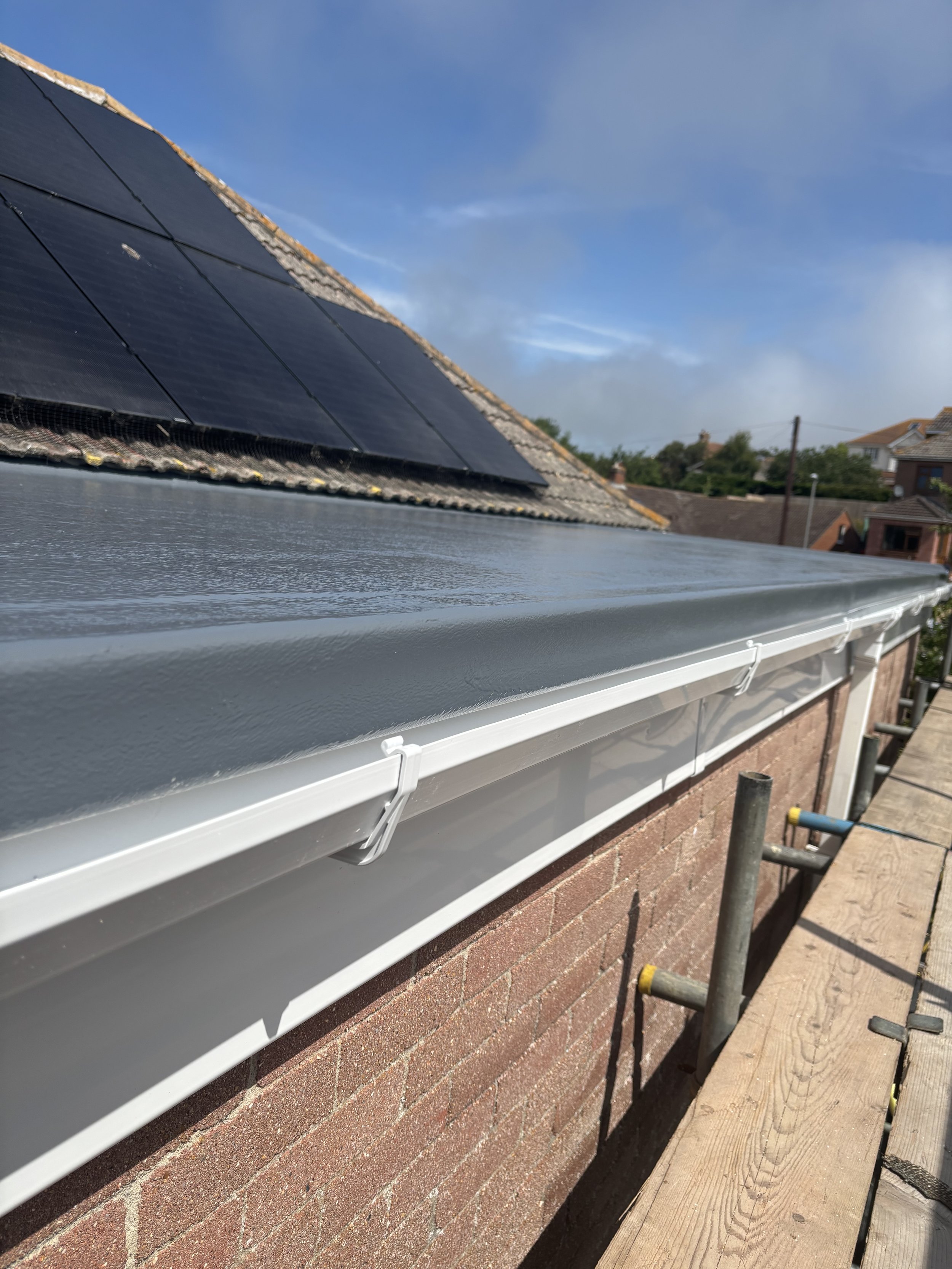 View of a roof with solar panels and a gutter system, side of a brick building, cloudy sky.