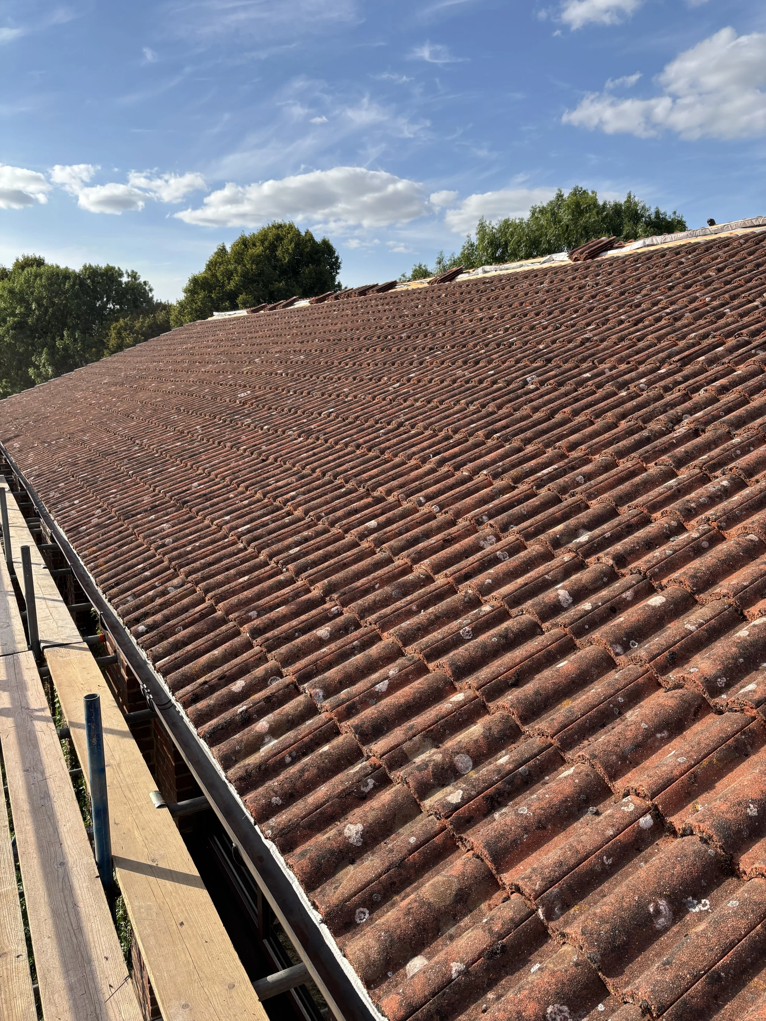 A tiled roof being repaired or under construction, with scaffolding on the side and a blue sky with some scattered clouds overhead.