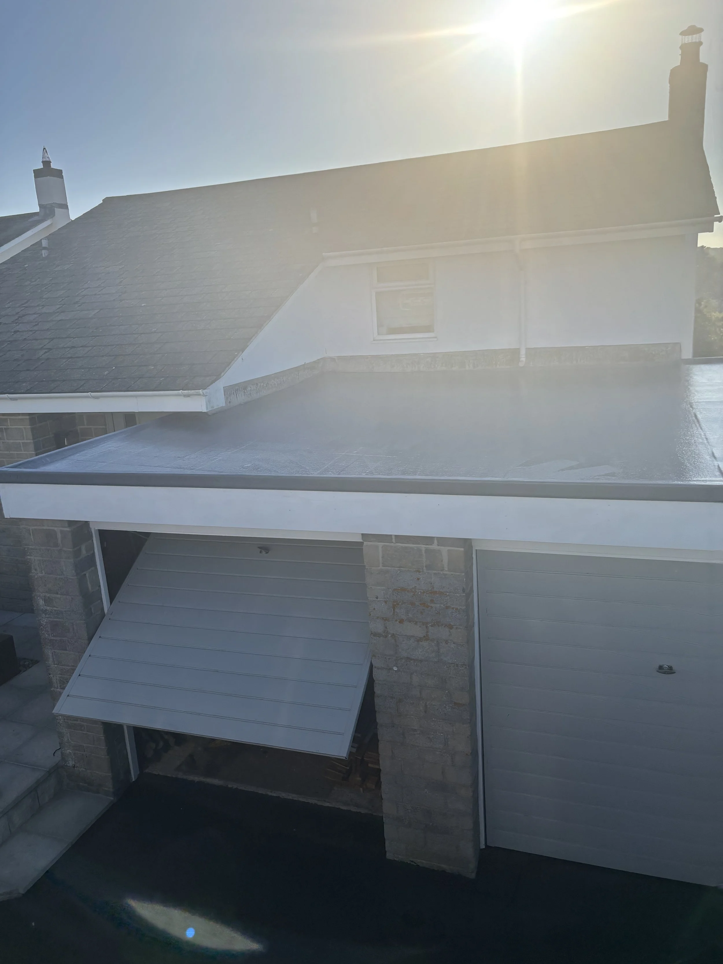 A residential house with a garage and a small window, sun shining brightly behind the roof, creating a lens flare and overexposure in the upper part of the image.