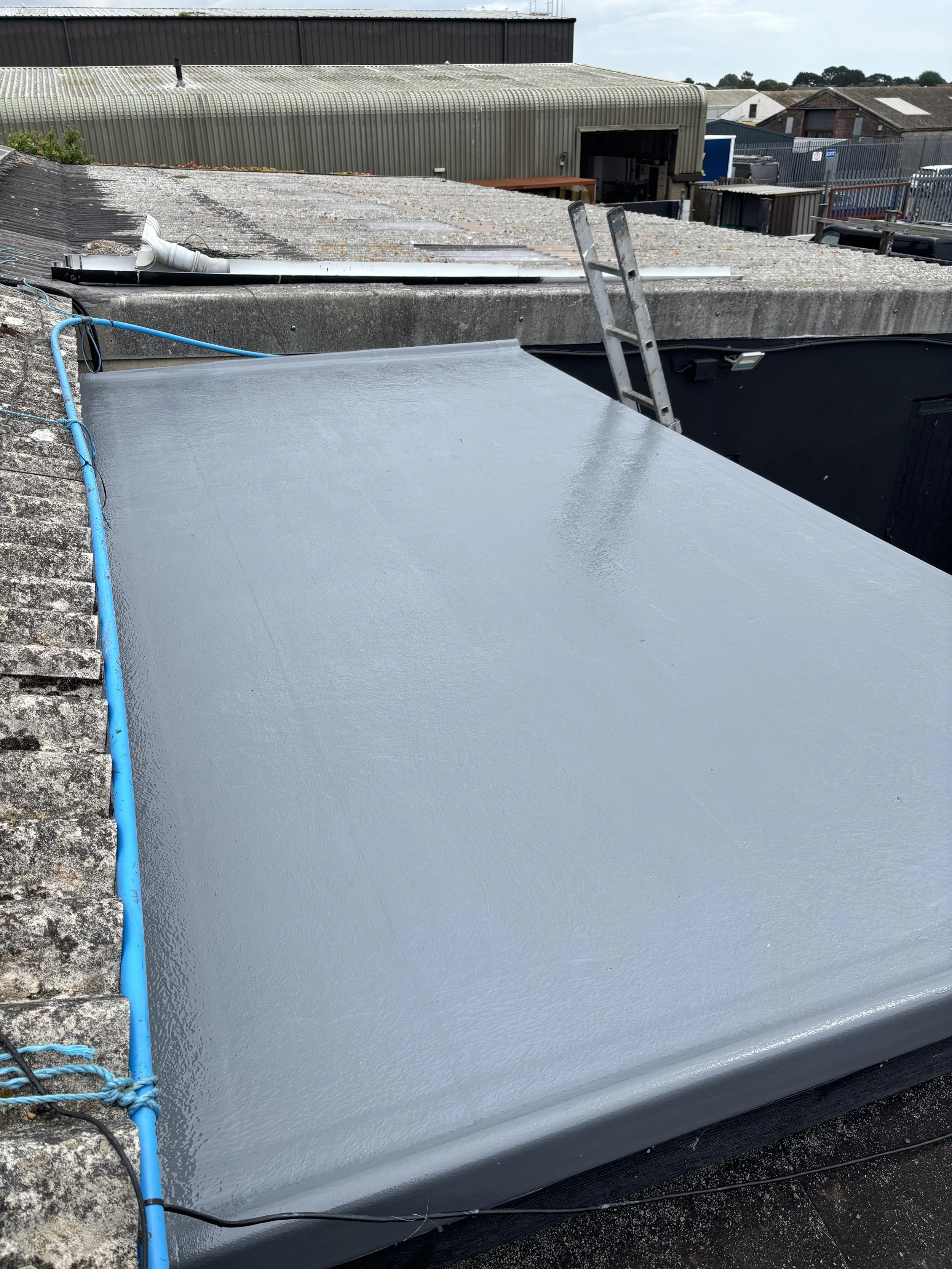 A newly painted flat roof with a gray coating, a small ladder, and an exposed roof gutter.