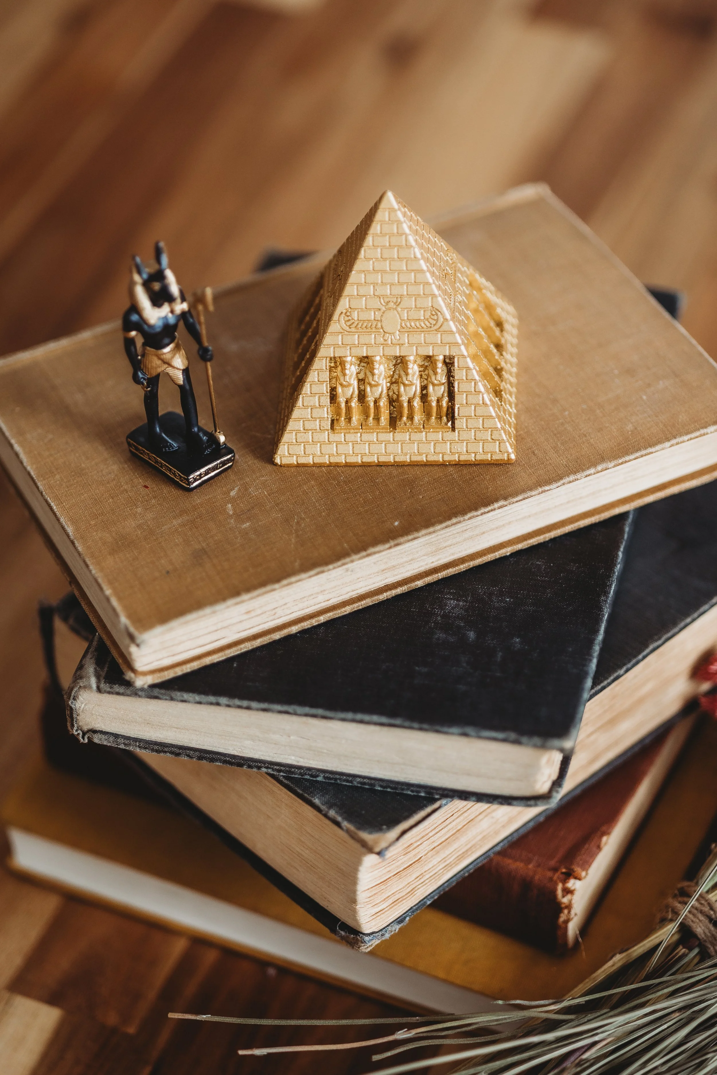 A stack of vintage books with a small figurine of an Egyptian soldier and a miniature golden Egyptian pyramid on top.