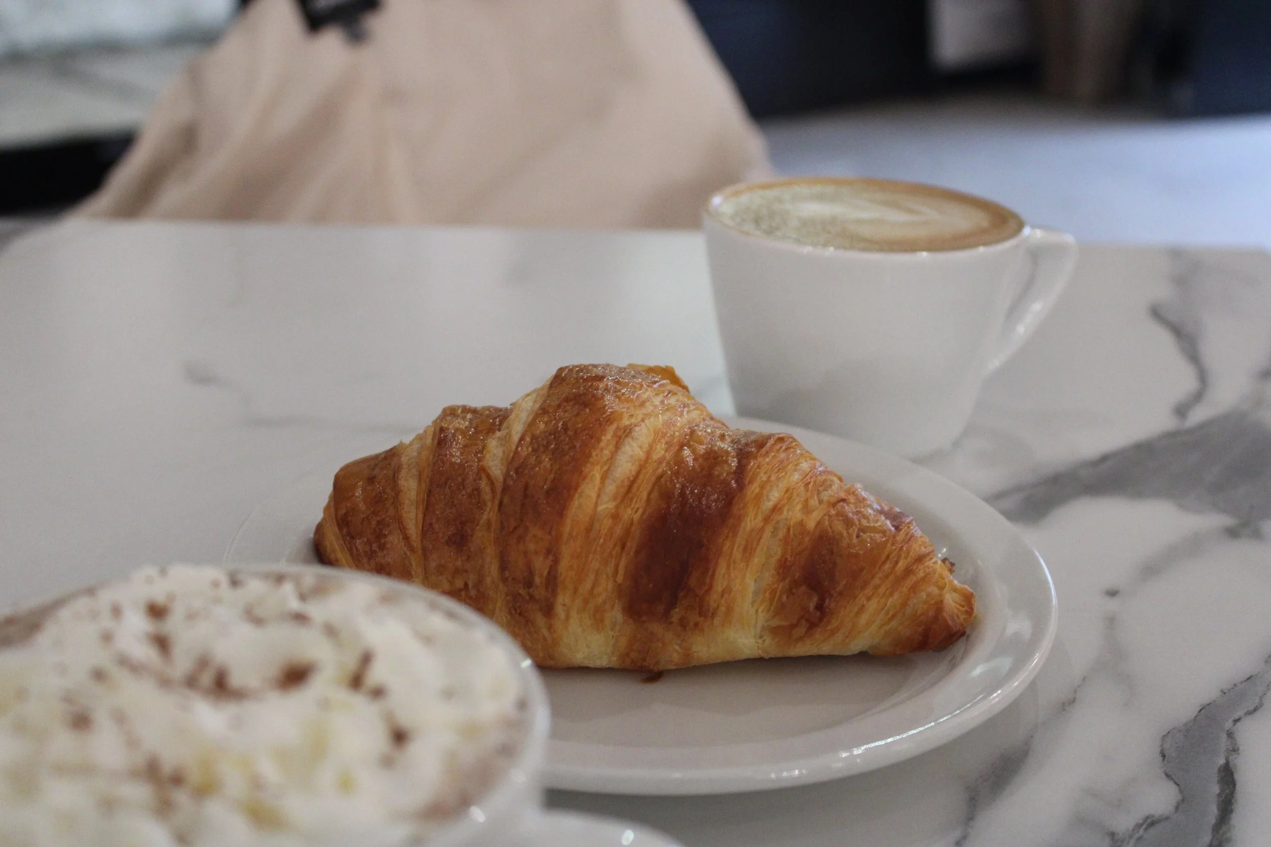 A hot chocolate in the front and a croissant and a cappuccino from Crown and Press in Hamilton, Ontario.