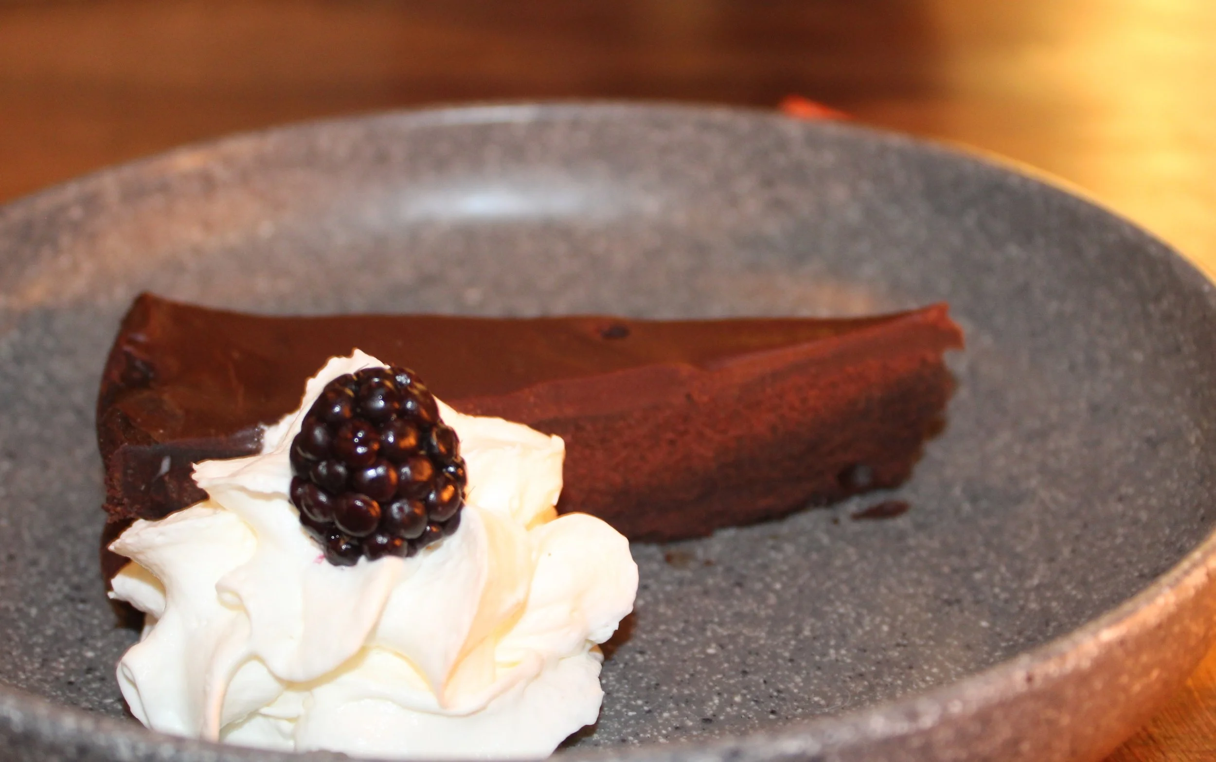 A chocolate cake with whipped cream and a blackberry on top from The Planl.