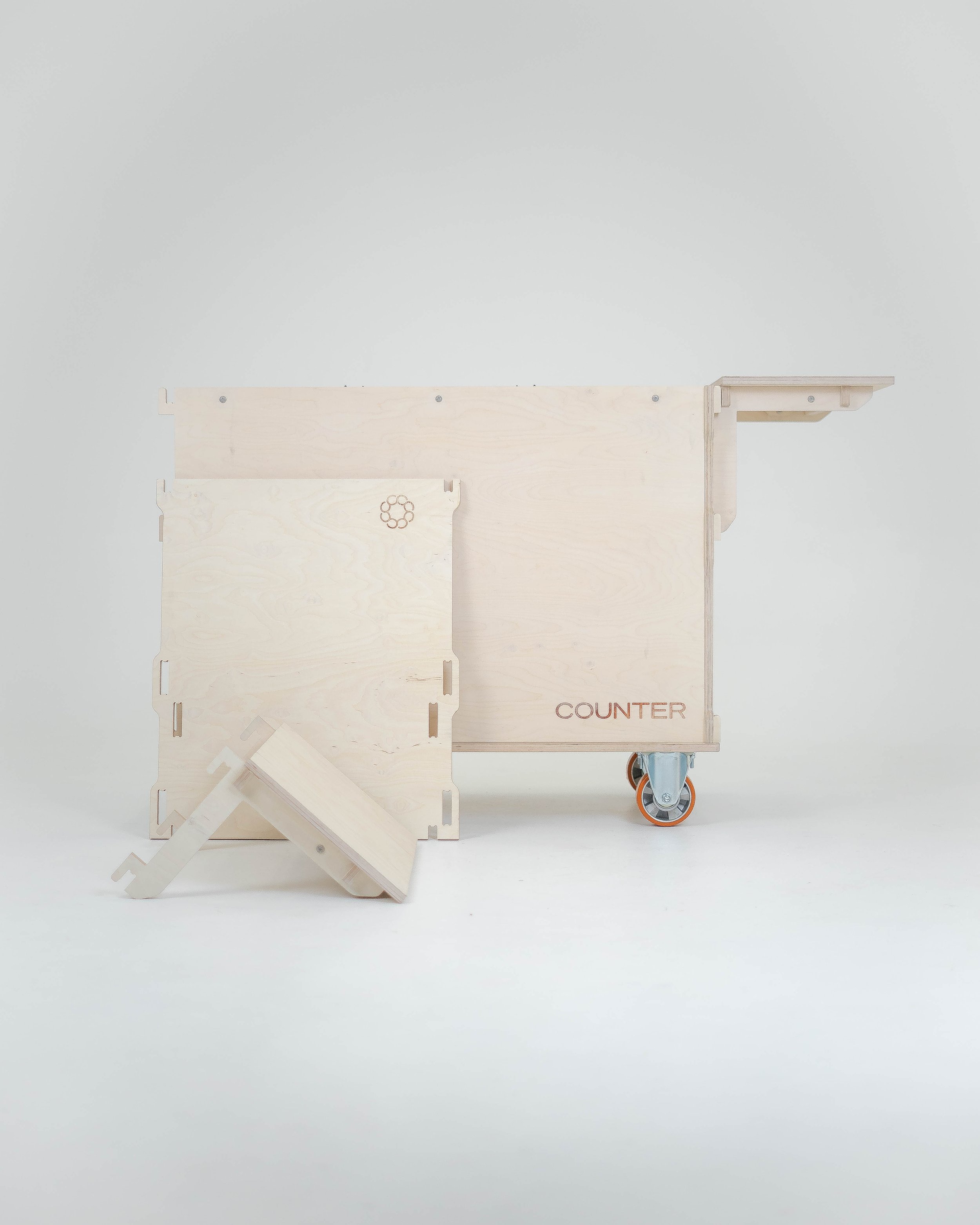Unassembled wooden counter with wheels, including a top surface, a side panel, and a small angled piece, all made of light-colored wood.