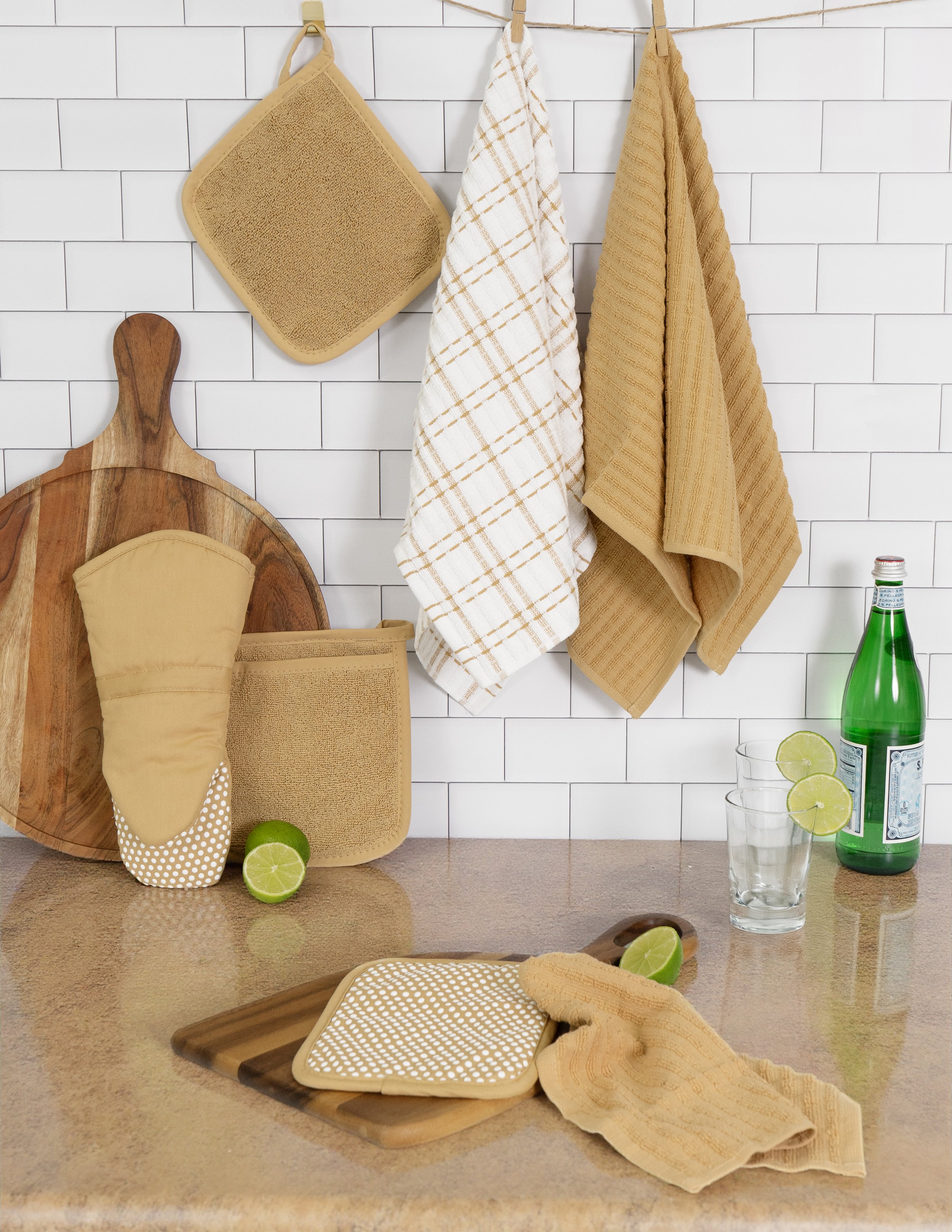 Kitchen scene with hanging towels, cutting boards, lime slices, a bottle of sparkling water, and glasses on a countertop.