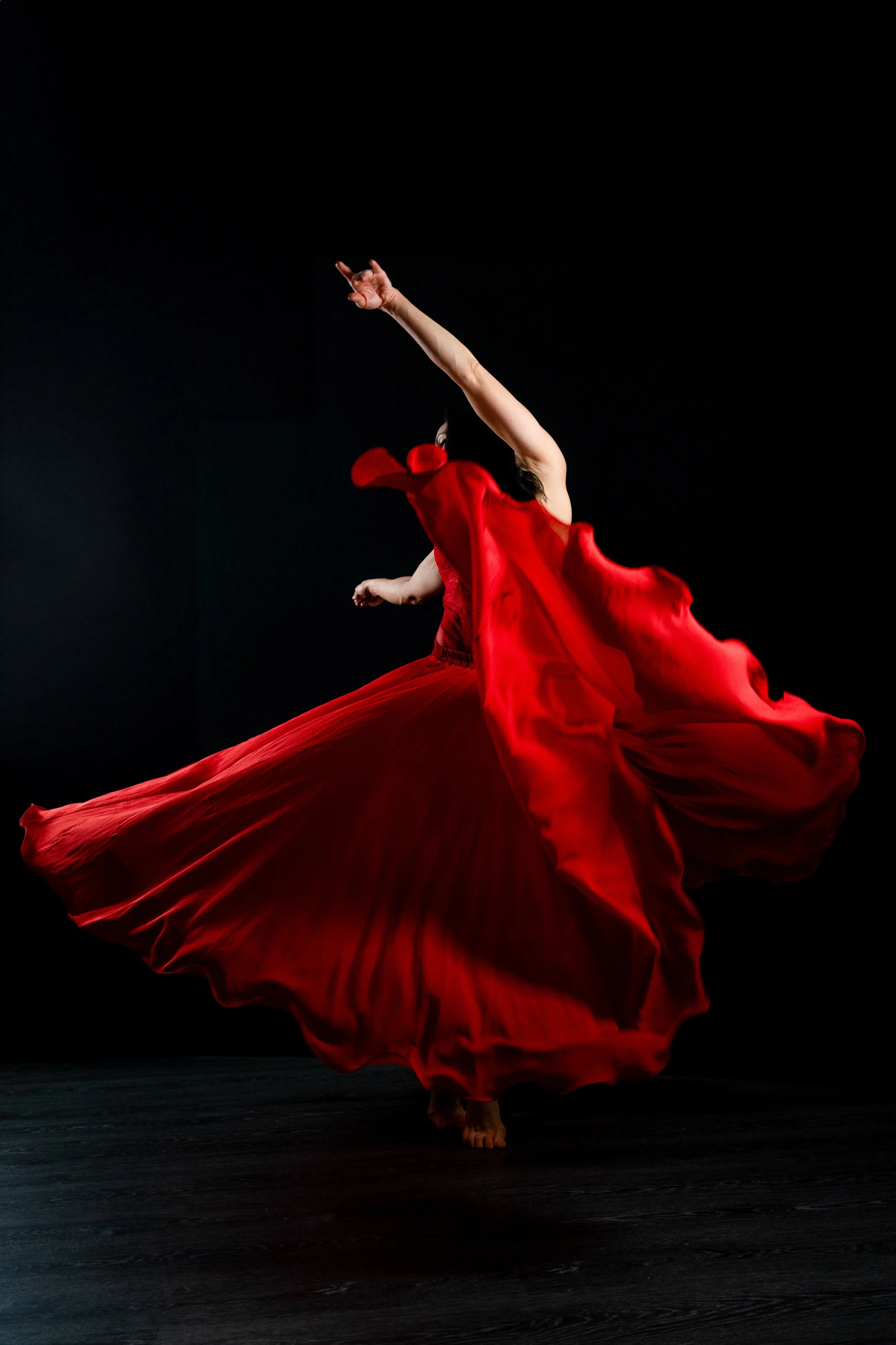 A dancer in a flowing red dress spinning or twirling on stage with a black background.