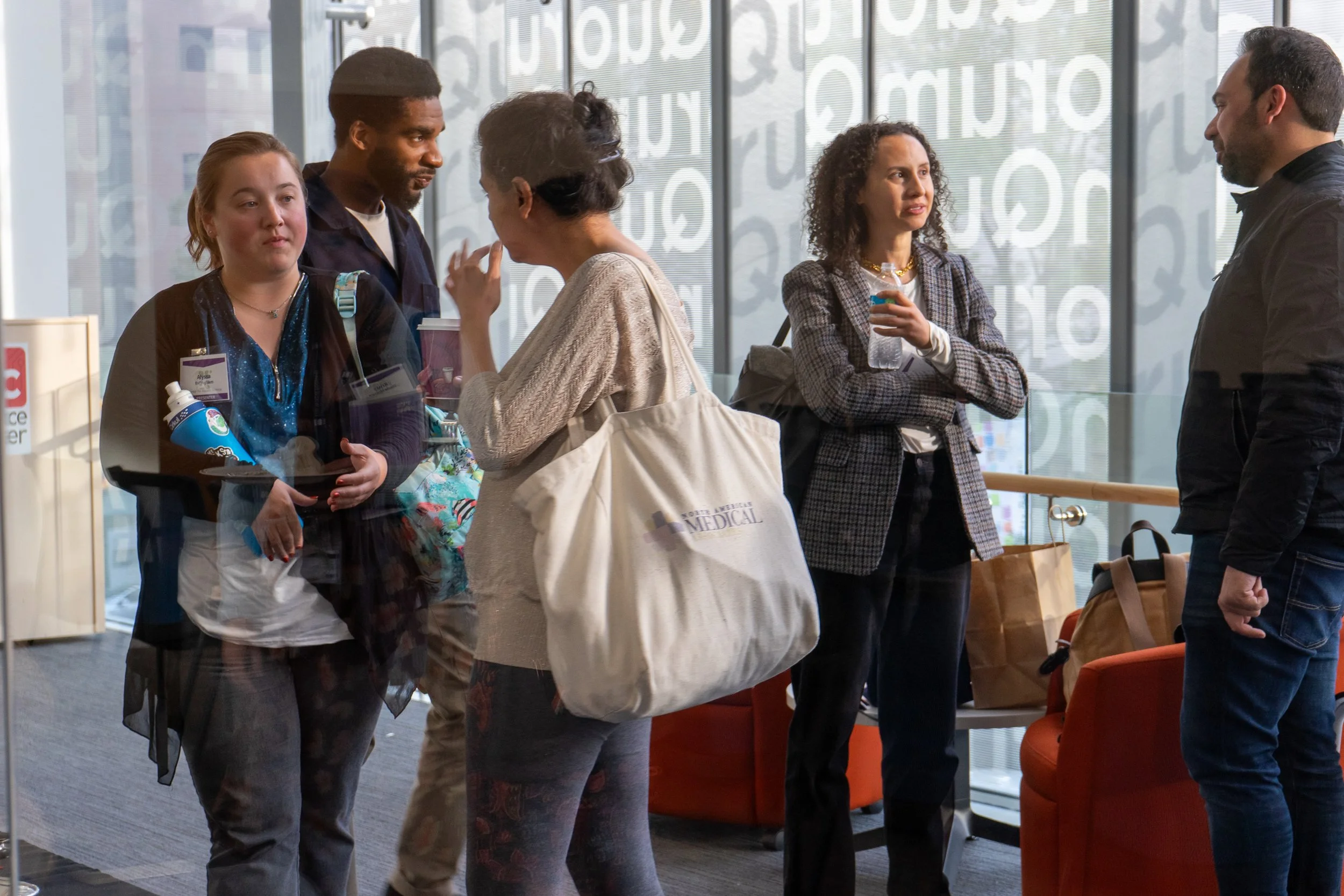 Group of people talking and waiting in a lobby or waiting area near large windows with geometric patterns