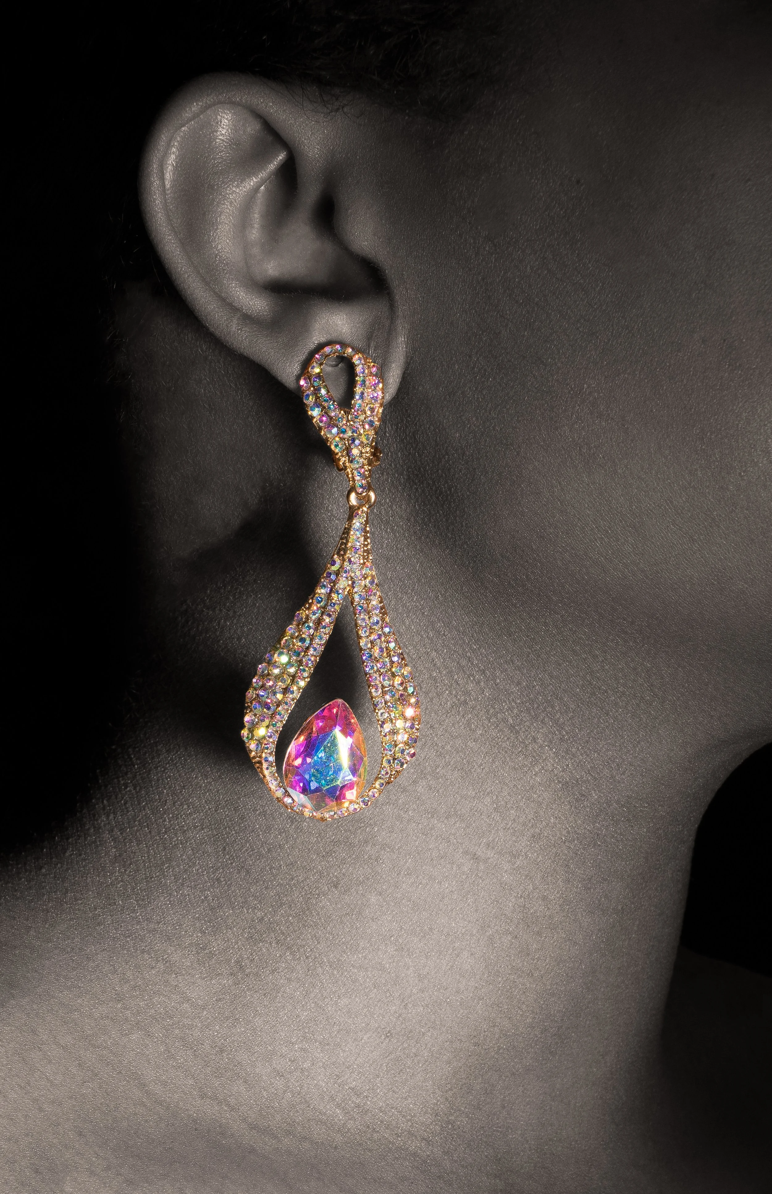 Close-up of a woman's ear wearing a large, teardrop-shaped, multicolored rhinestone earring.