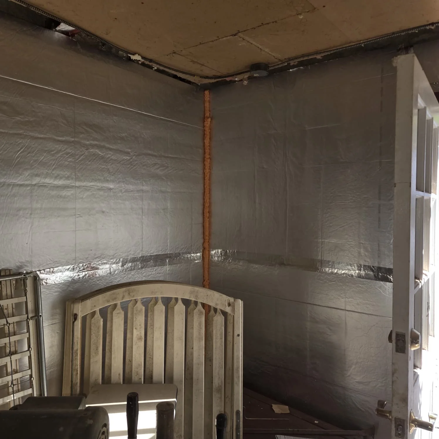 Interior of a room under renovation with of wall insulation and a door with outdoor light shining in.