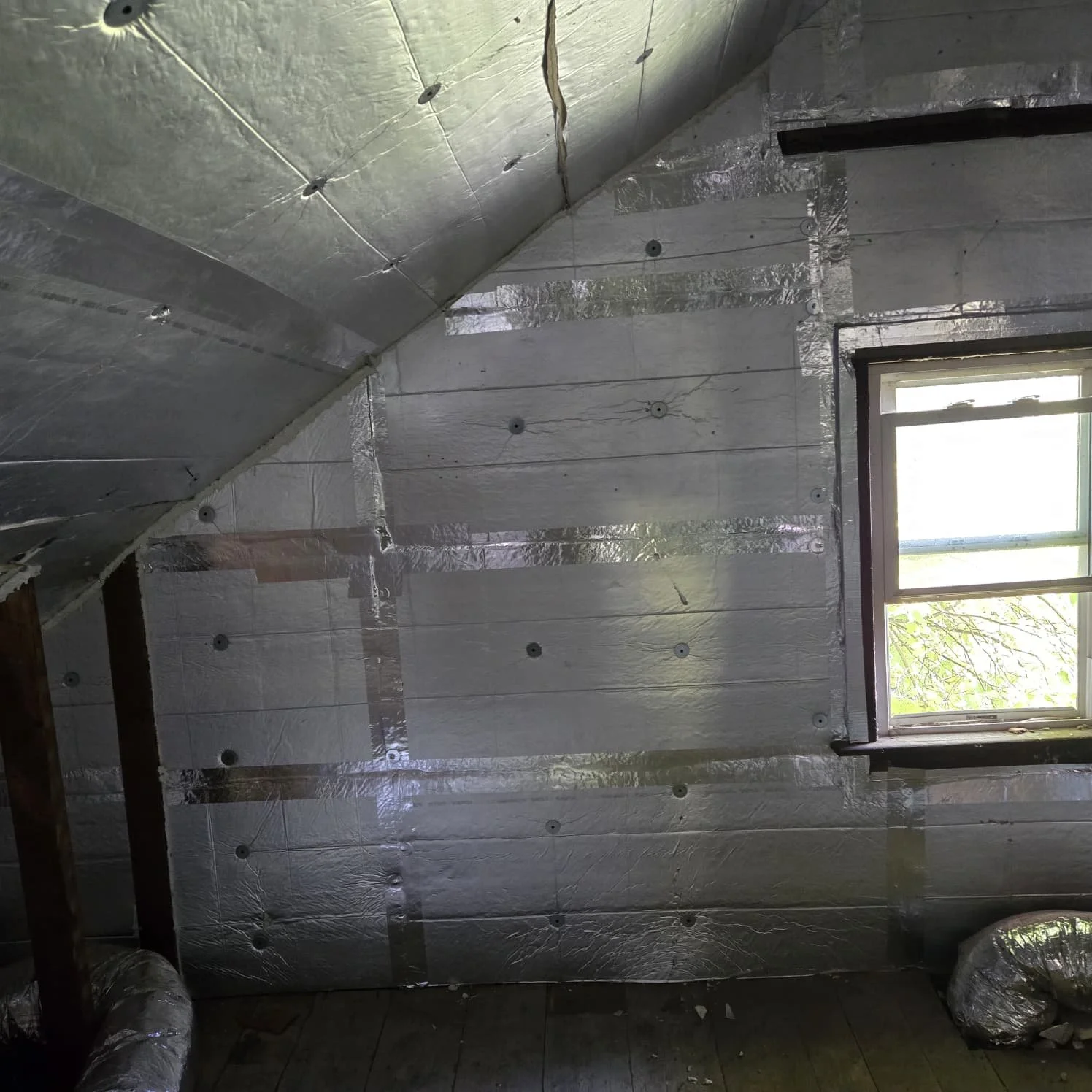 Insulated wall with multiple foam boards and wiring, above a window with a view of trees outside.