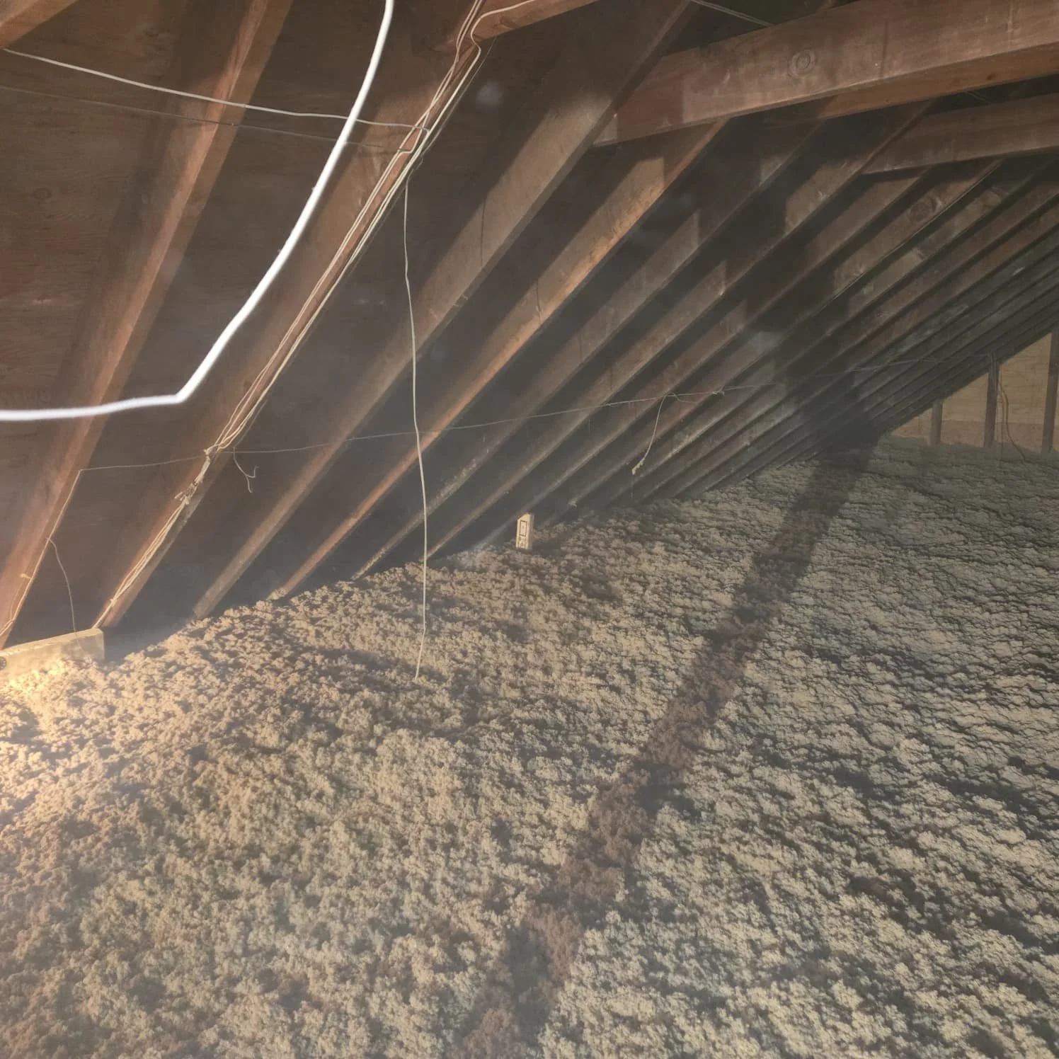 Attic space with exposed wooden beams and spray foam insulation on the floor.