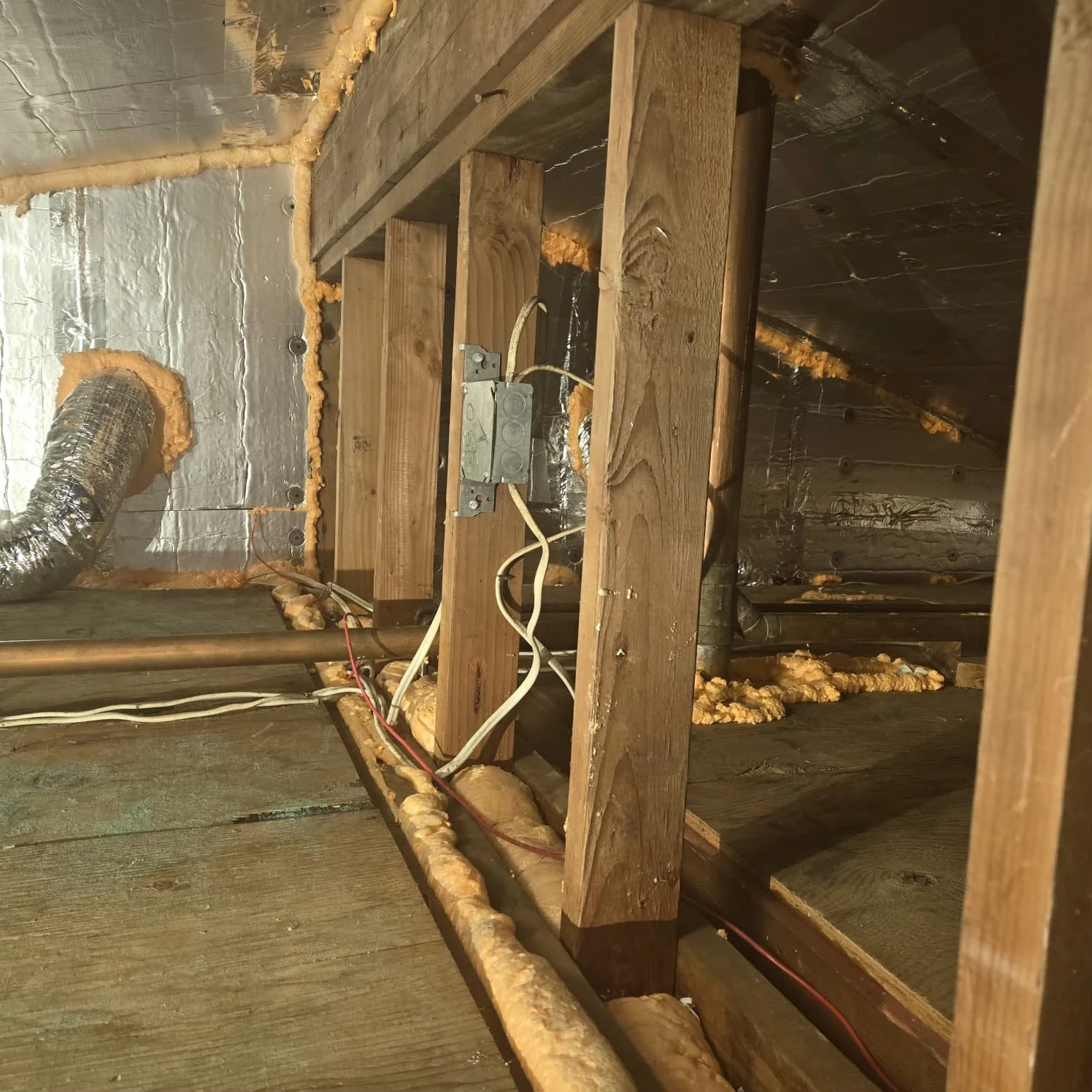 Indoor view of a construction or renovation site showing electrical wiring and insulation with exposed wooden framing and foil insulation