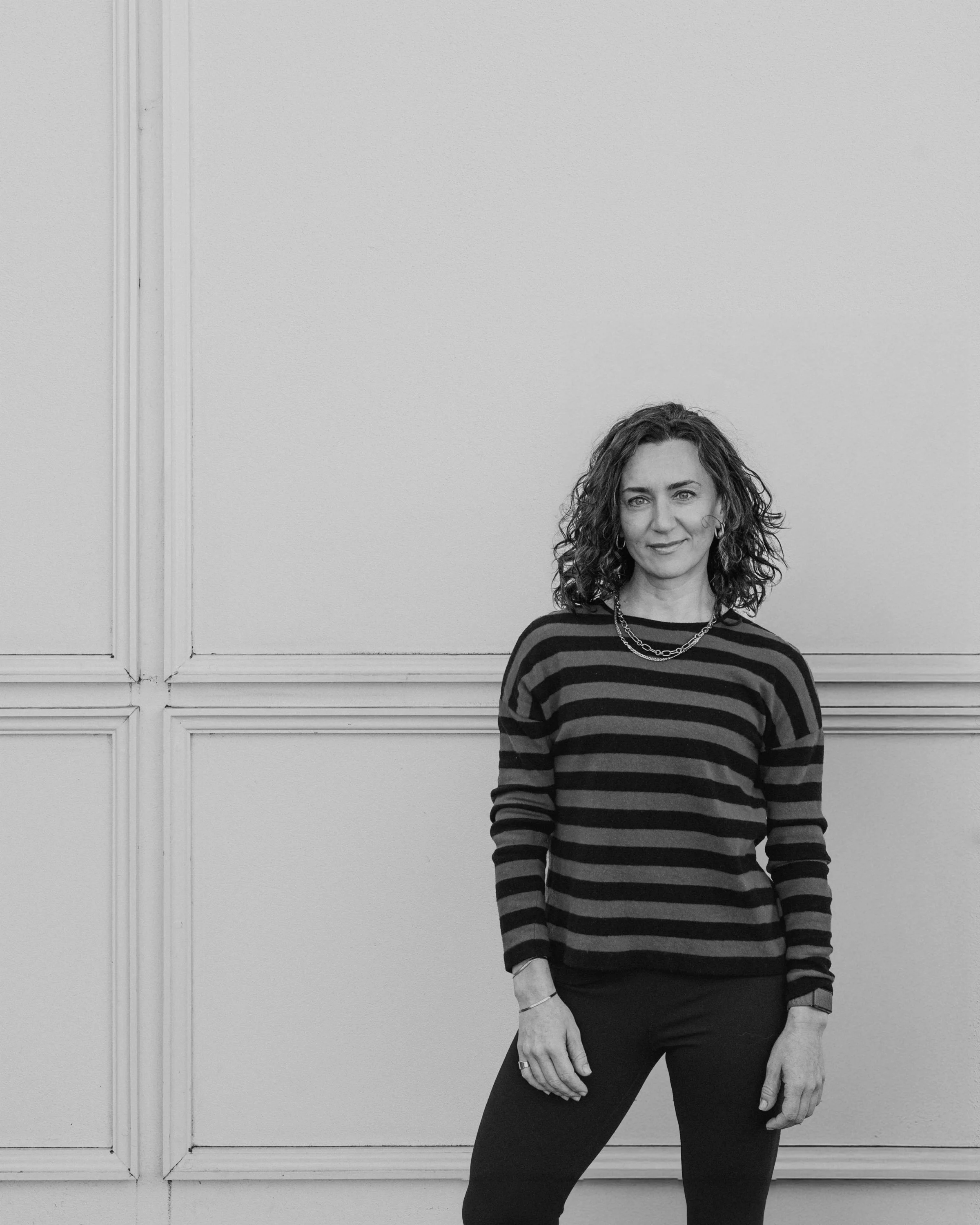 Person wearing a green and black striped sweater standing against a beige wall.