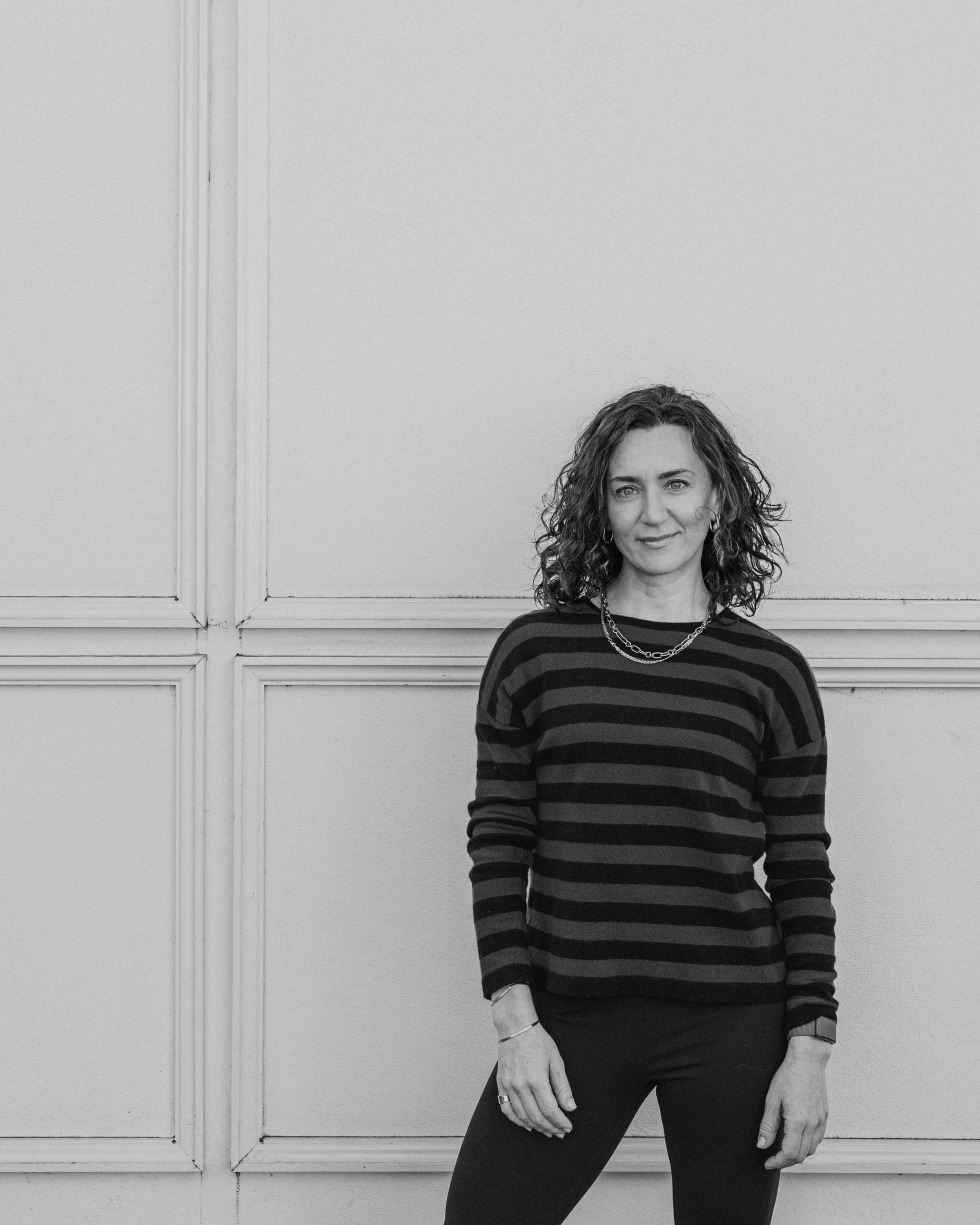 Person wearing a green and black striped sweater standing against a beige wall.