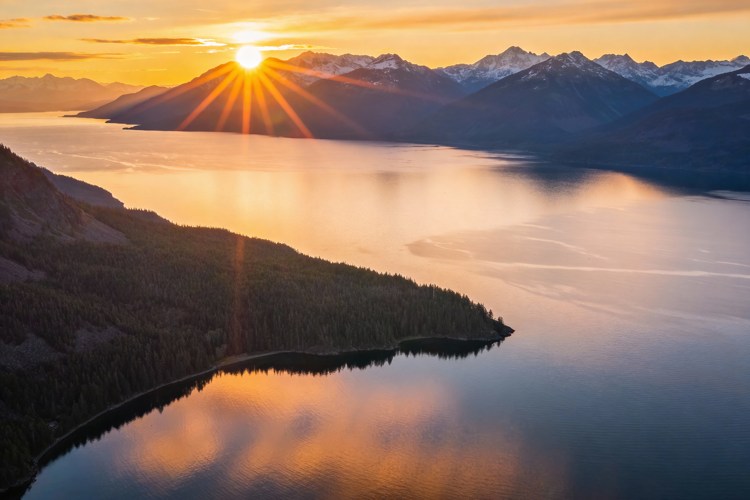 Sunset over Chilko Lake with snow-capped peaks reflecting orange and purple sky, British Columbia