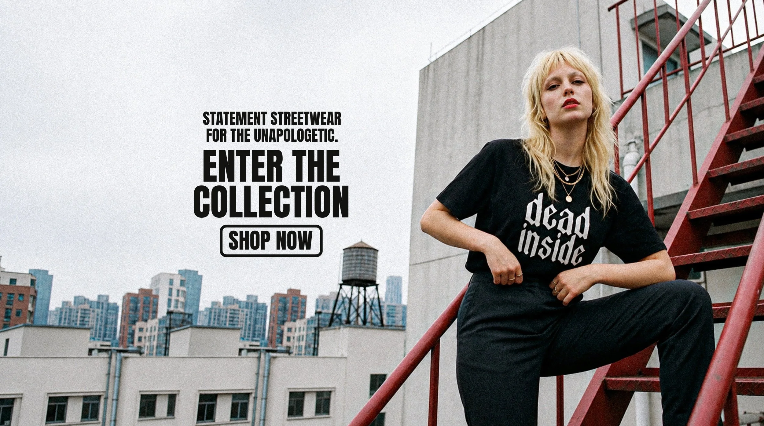 A young woman with blonde hair, wearing a black t-shirt with white text, sitting on a red fire escape ladder on a rooftop with a cityscape background. The t-shirt reads 'dead inside'.