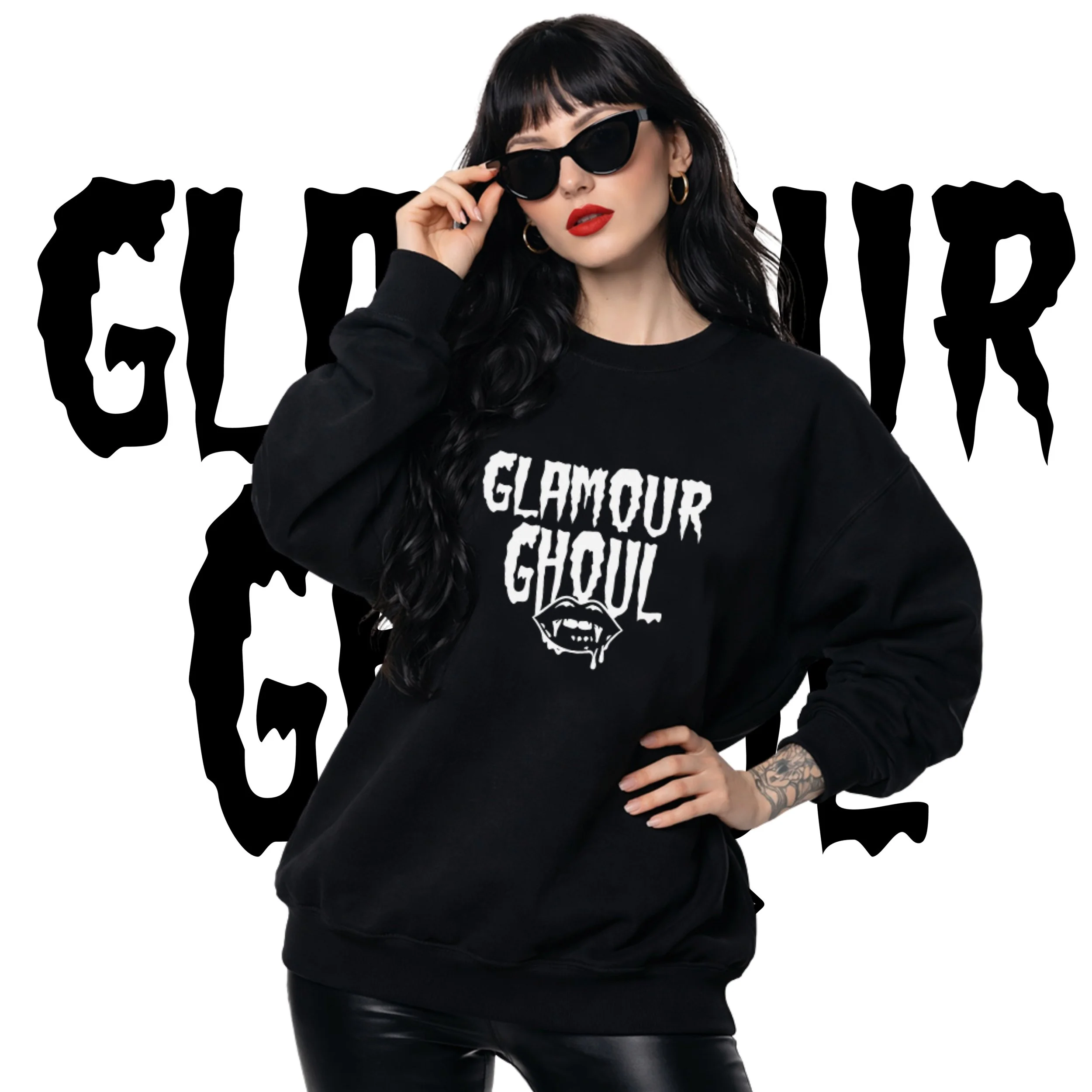 A woman with long black hair and tattoos wearing sunglasses, a black sweatshirt with 'Glamour Ghoul' and graphic lips, standing in front of a white background with 'Glamour Ghoul' text.