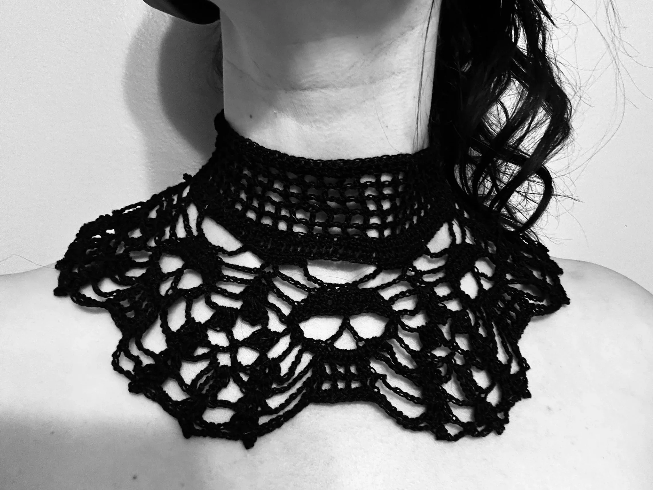 Black lace choker necklace on a person's neck and shoulders, with part of their dark, curly hair visible.